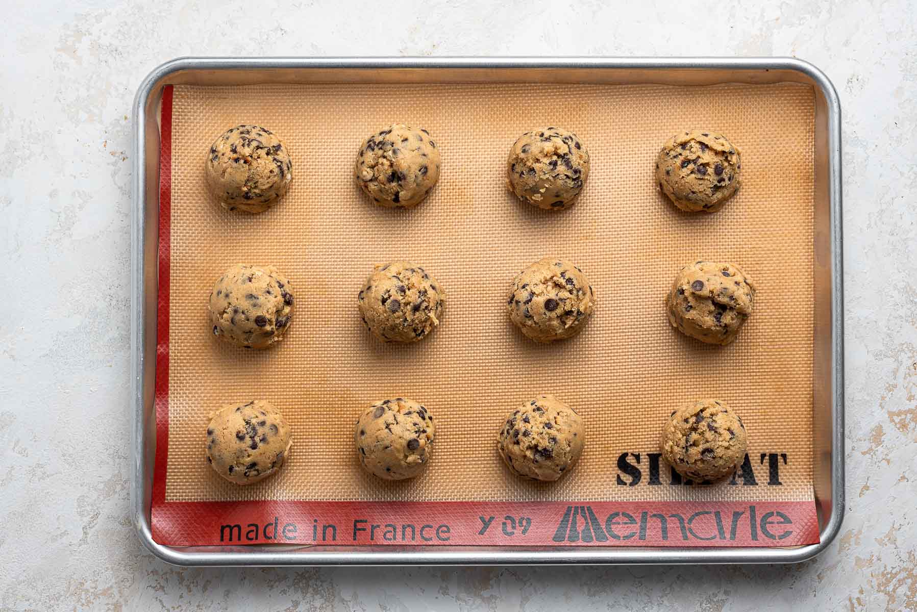 Raw cookie dough balls on baking sheet with silpat.