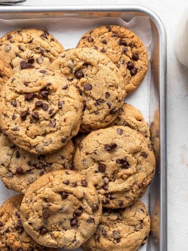 Pan of stacked chocolate chip cookies with walnuts on white table.