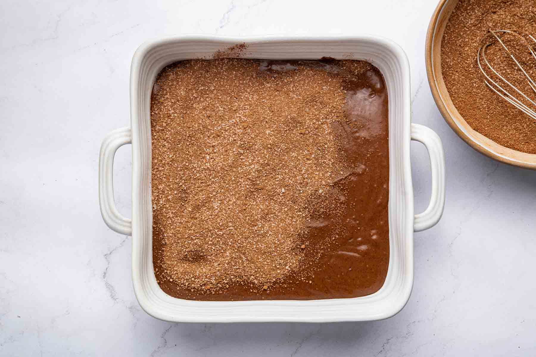 Sprinkling brown dry ingredients over wet batter in a square dish.