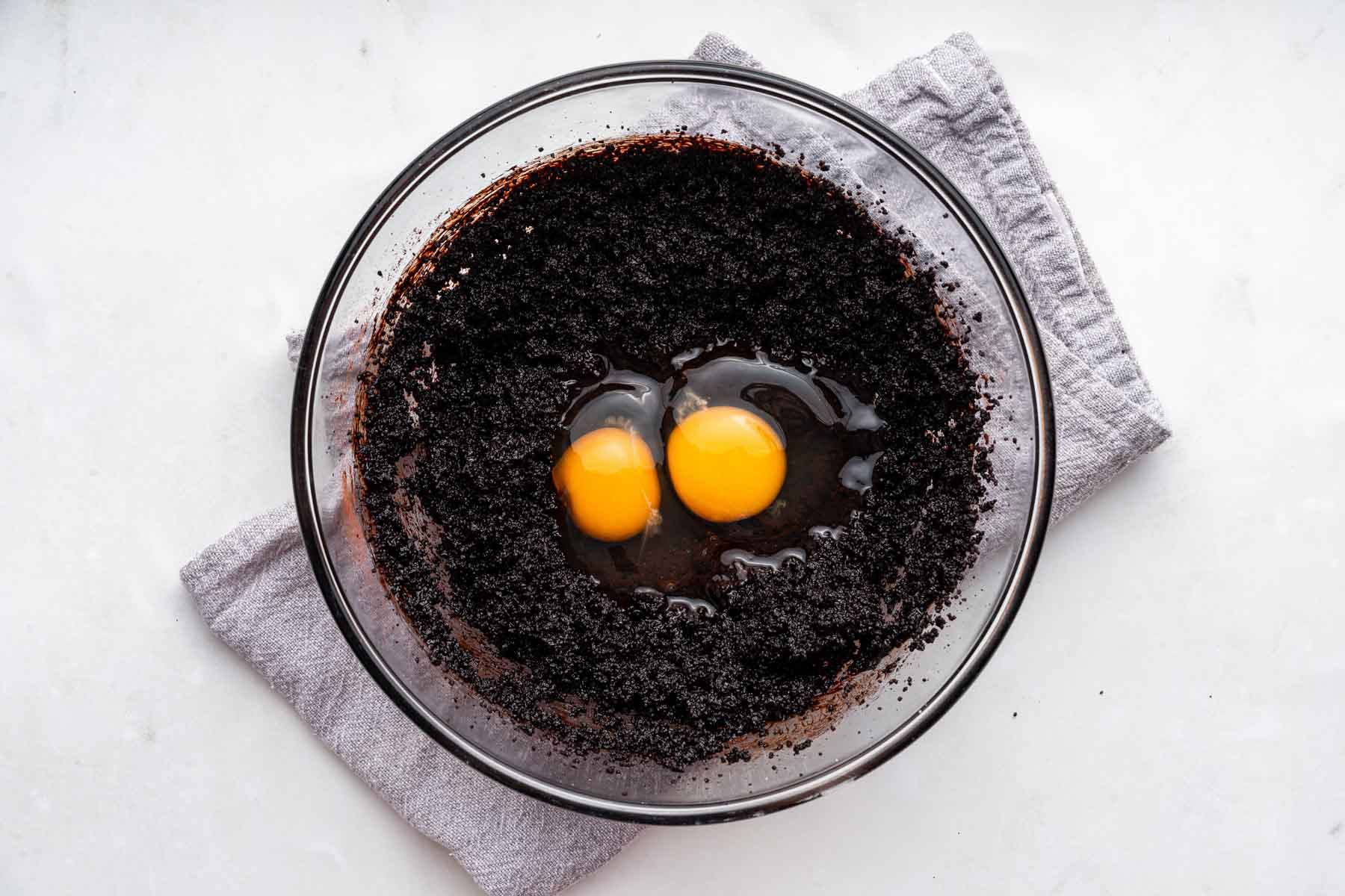 Dark brown batter with two raw eggs on top in bowl.
