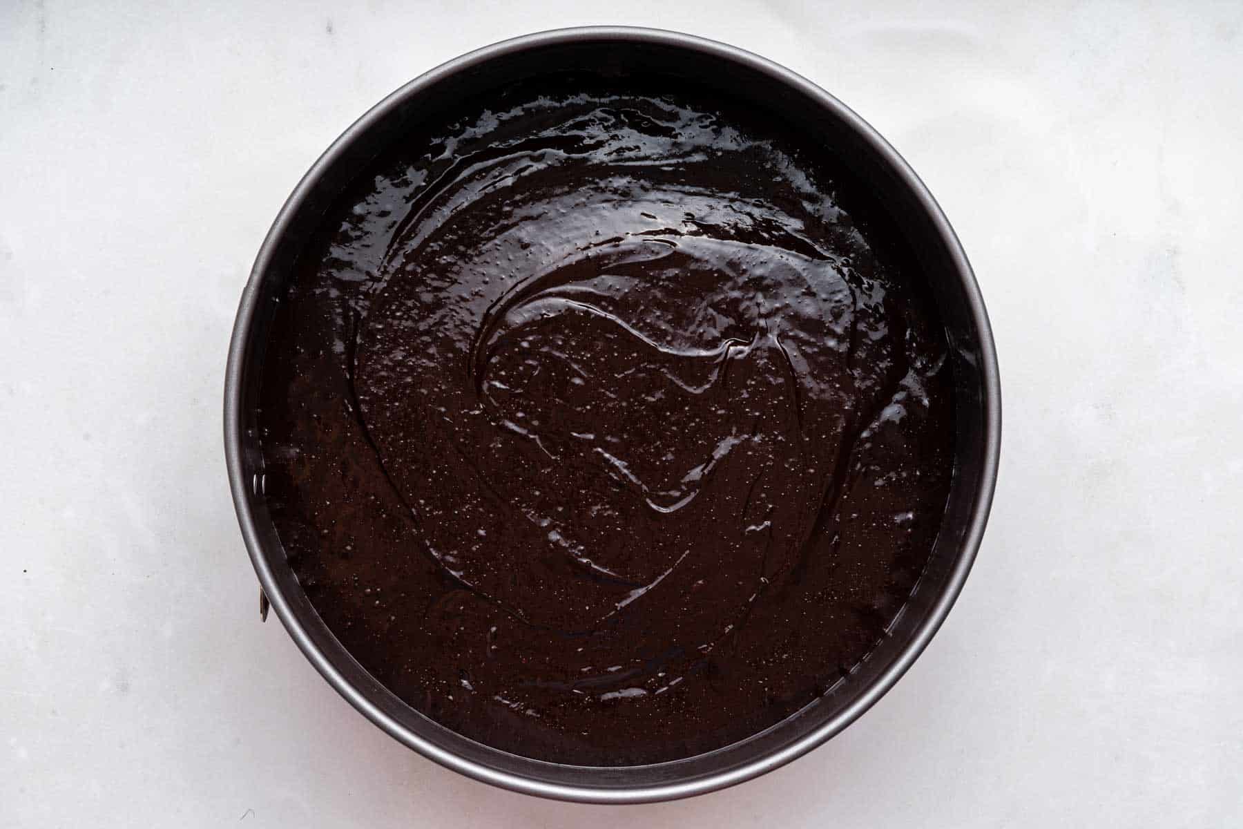 Raw brownie batter in a round cake pan.
