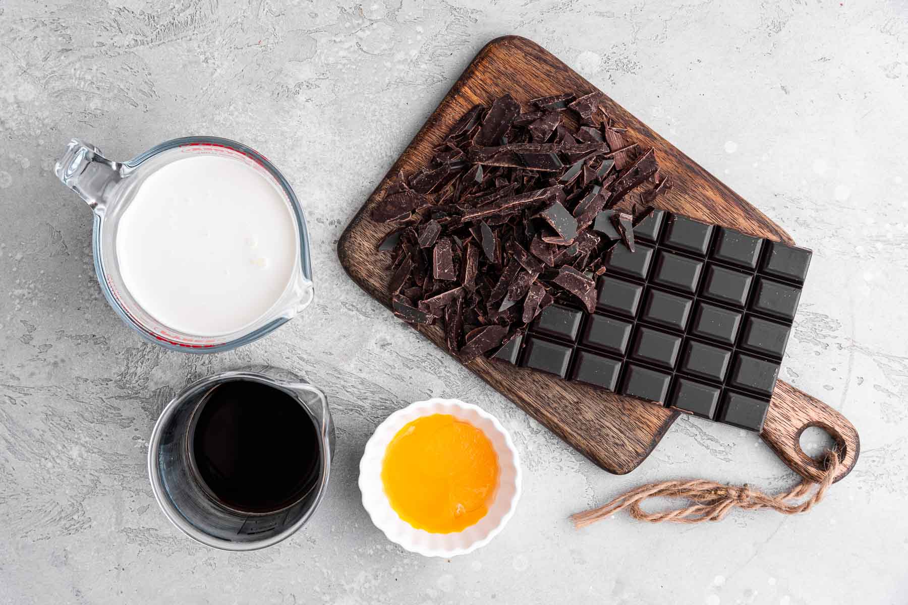 Chocolate bar, cream, coffee, and egg yolk on grey counter.