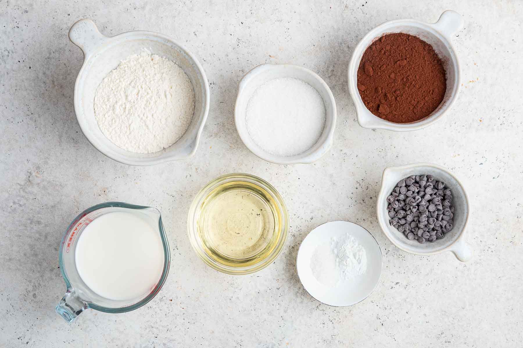 Smal bowls with flour, cocoa powder, oil, chocolate chips, and milk.