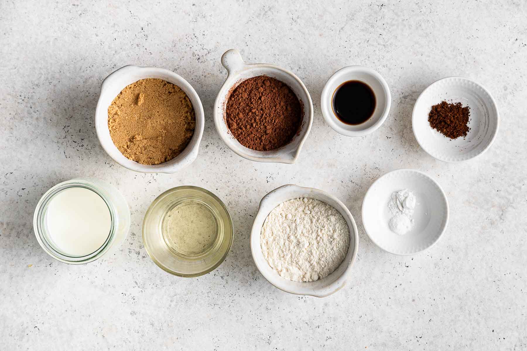 Ingredients for chocolate peanut butter cupcakes in small bowls on white counter.