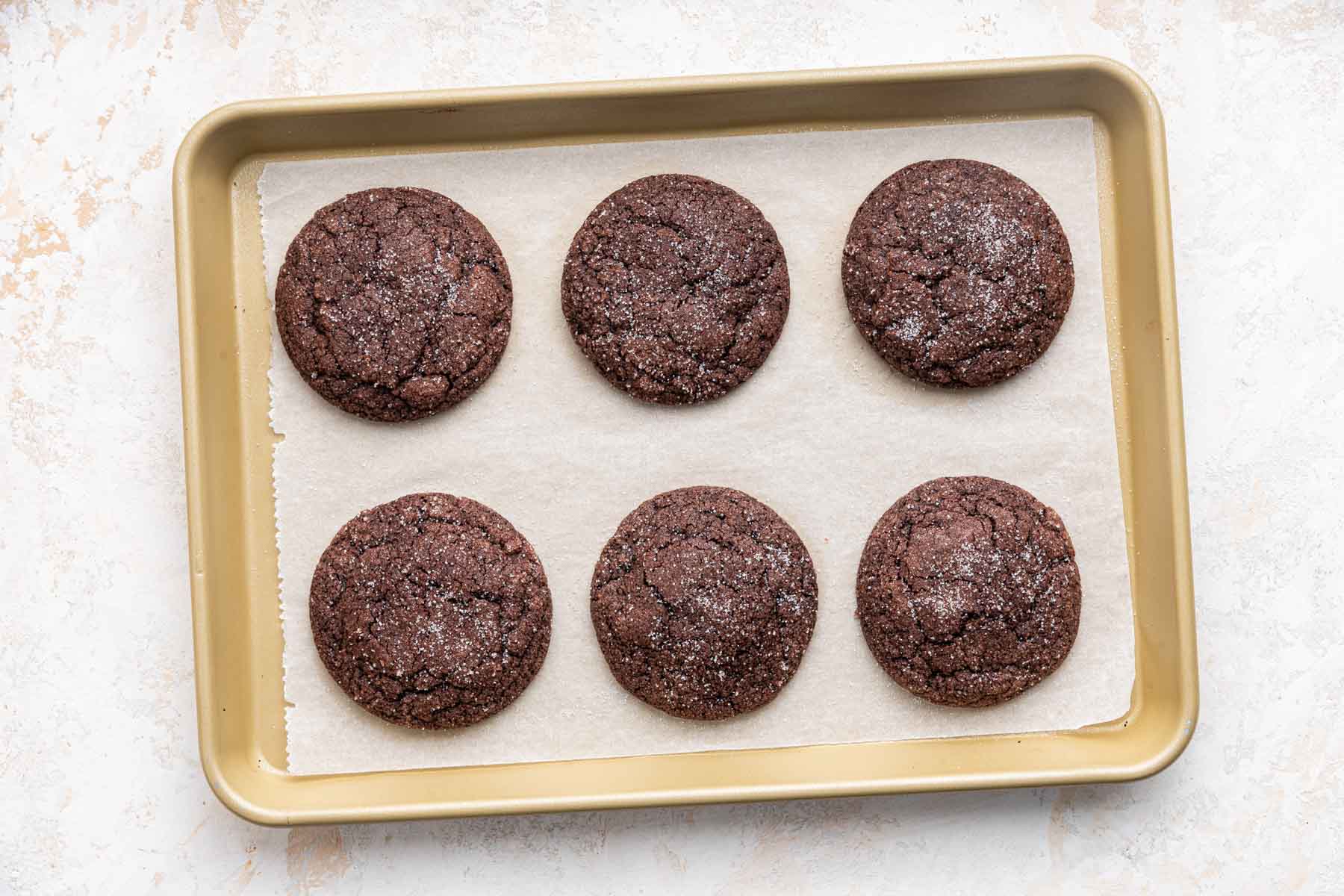 Six brown chocolate sugar cookies on a small cookie sheet.