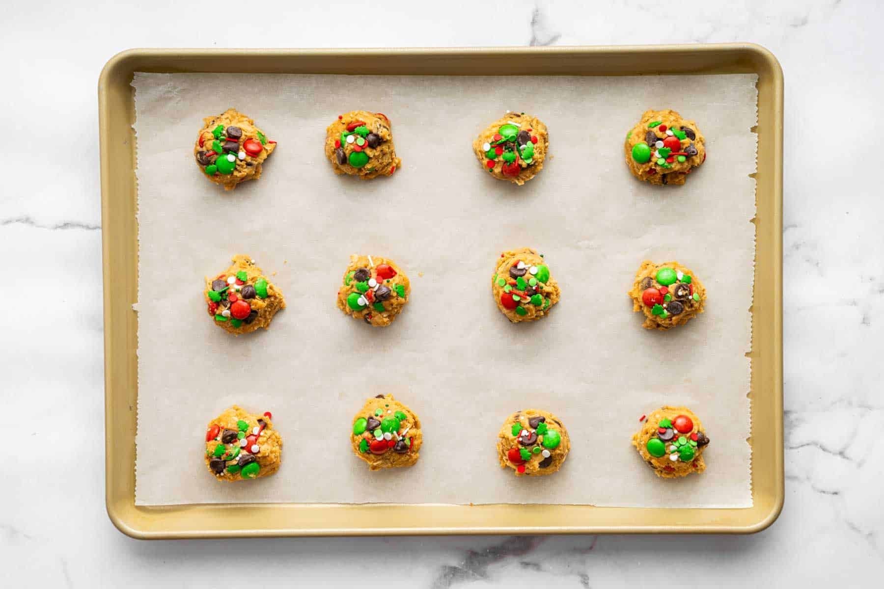 Twelve Christmas monster cookies on a sheet pan with extra sprinkles on top.