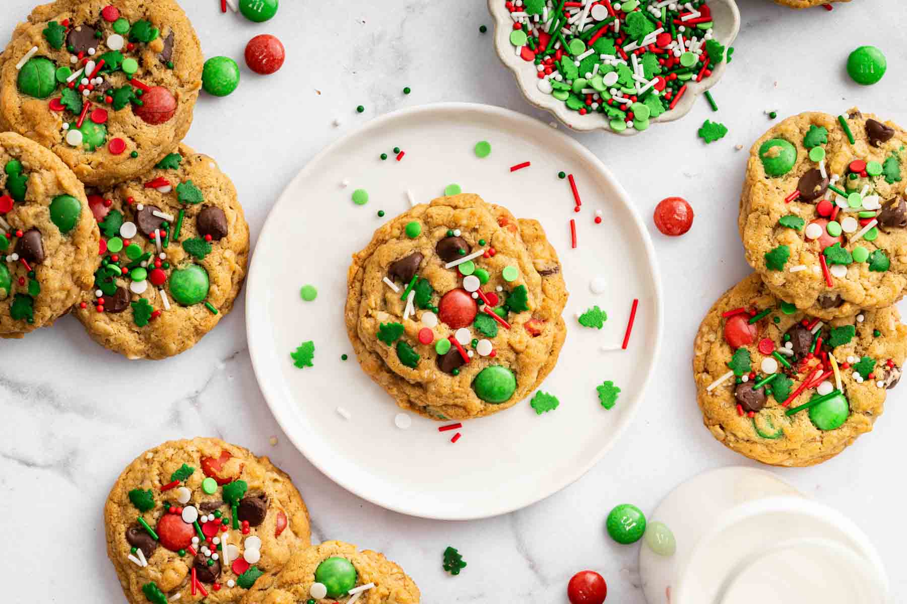 Horizontal image of colorful Christmas monster cookies on white plate with sprinkles everywhere.