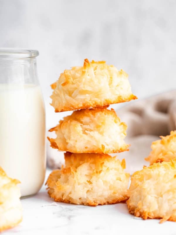 Three golden coconut macaroons stacked on each other next to milk.