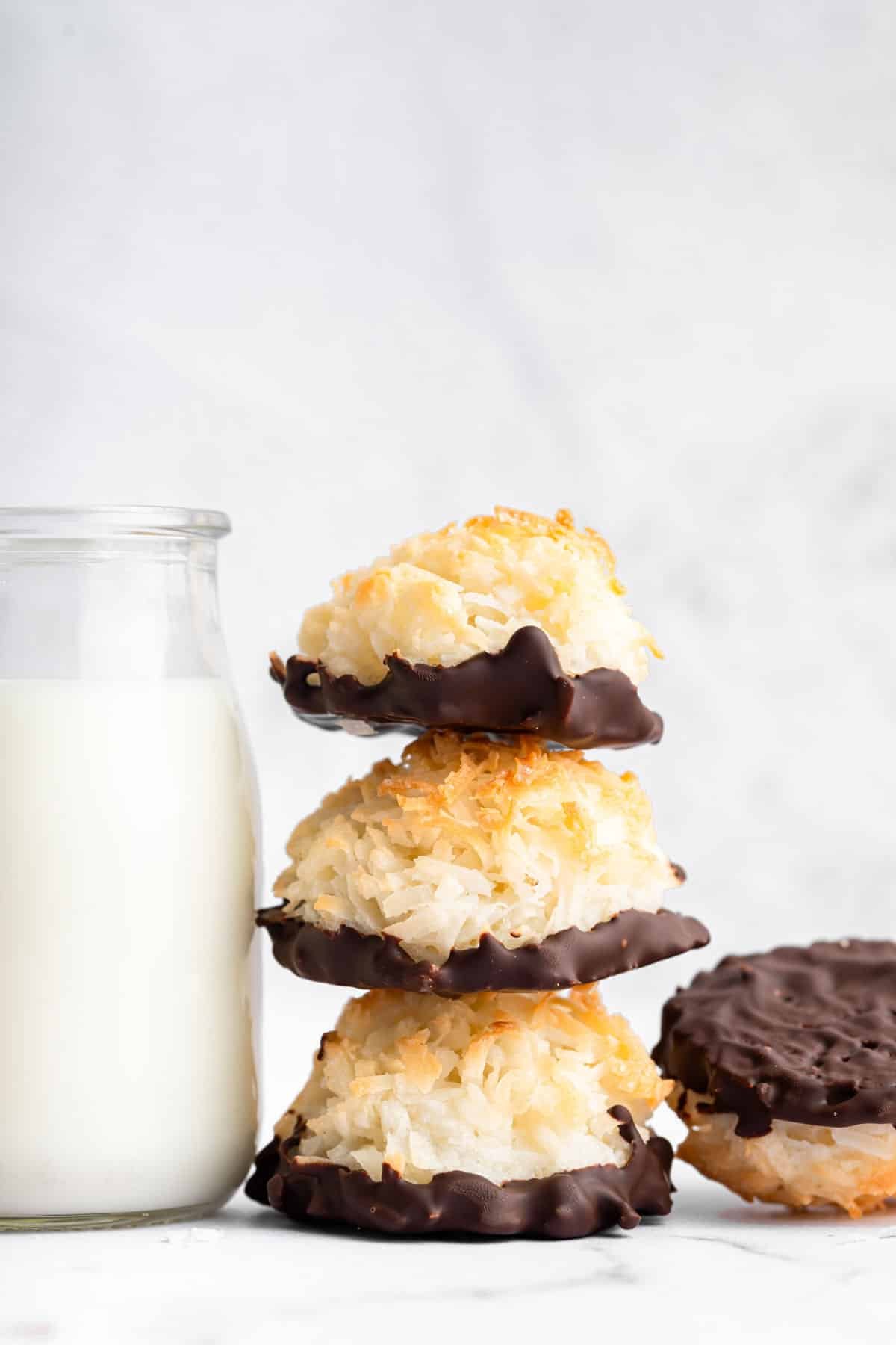Stack of coconut macaroons with chocolate bottoms next to glass of milk.