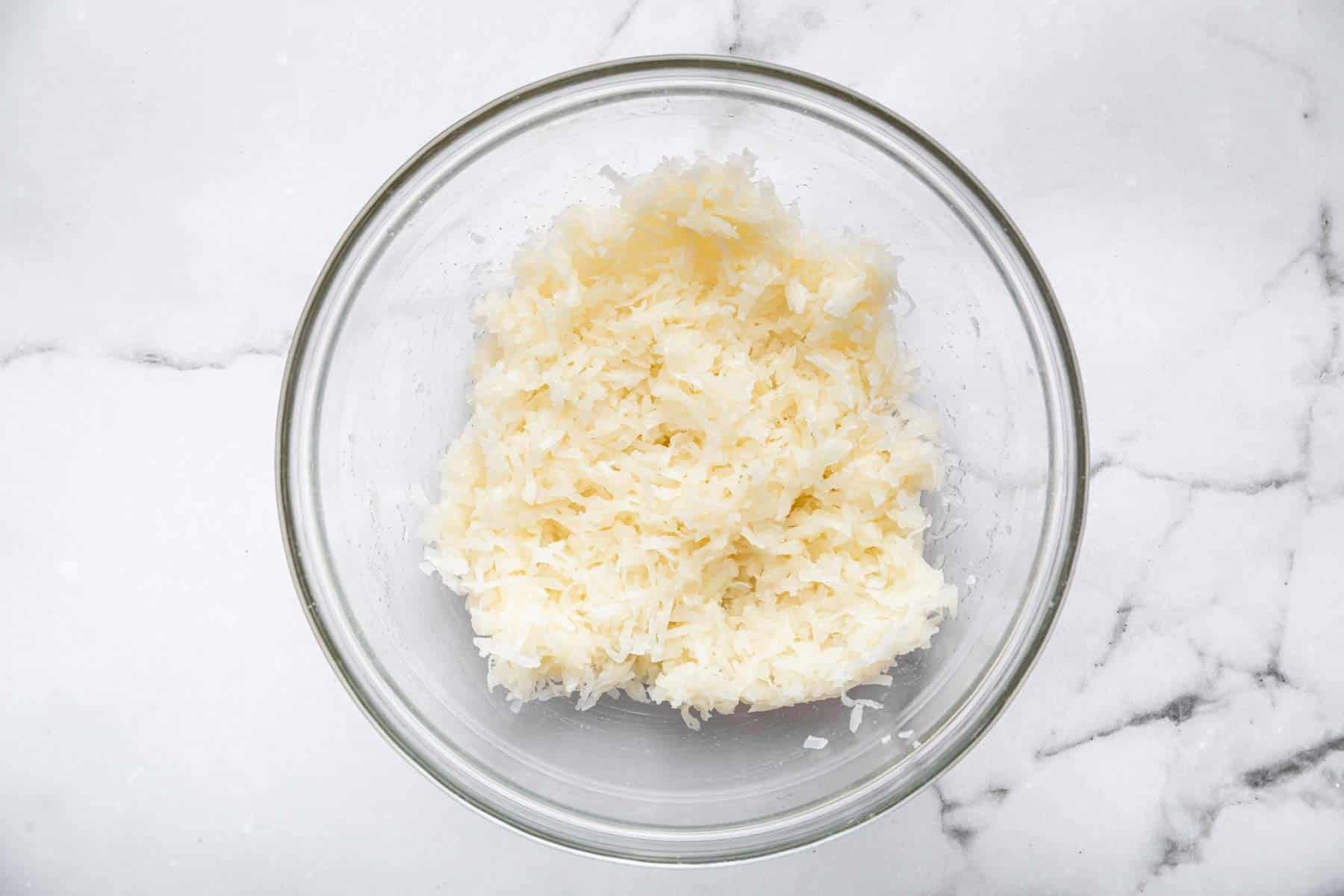 White, flaky wet cookie dough in a clear bowl before baking.