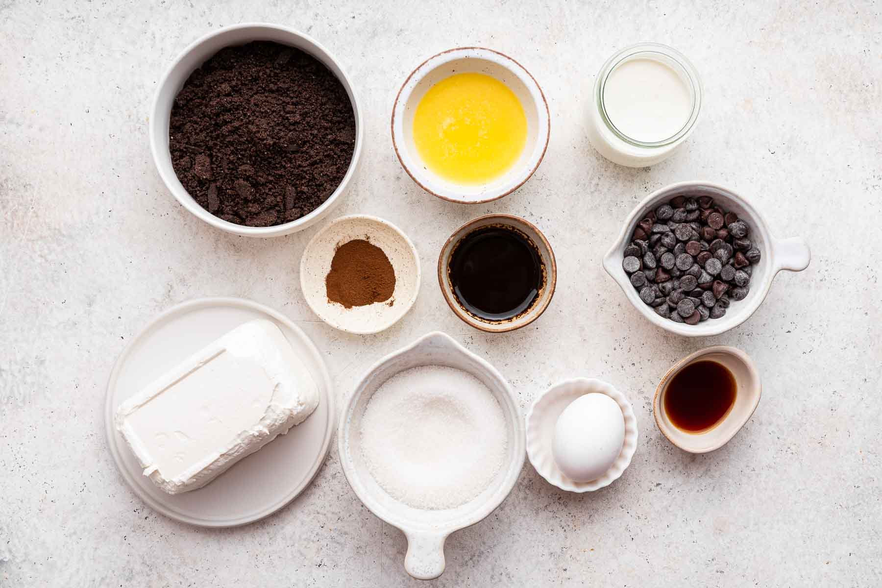 Small bowls of oreo crumbs, melted butter, cream cheese and chocolate chips.