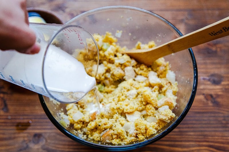 Hand pouring milk into cornbread dressing recipe bowl.