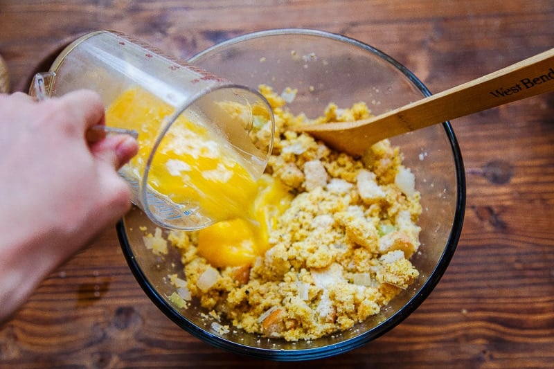 Hand pouring beaten eggs into bowl with southern cornbread dressing recipe ingredients.