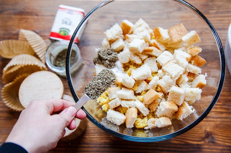 Hand adding spices to a bowl of bread cubes.