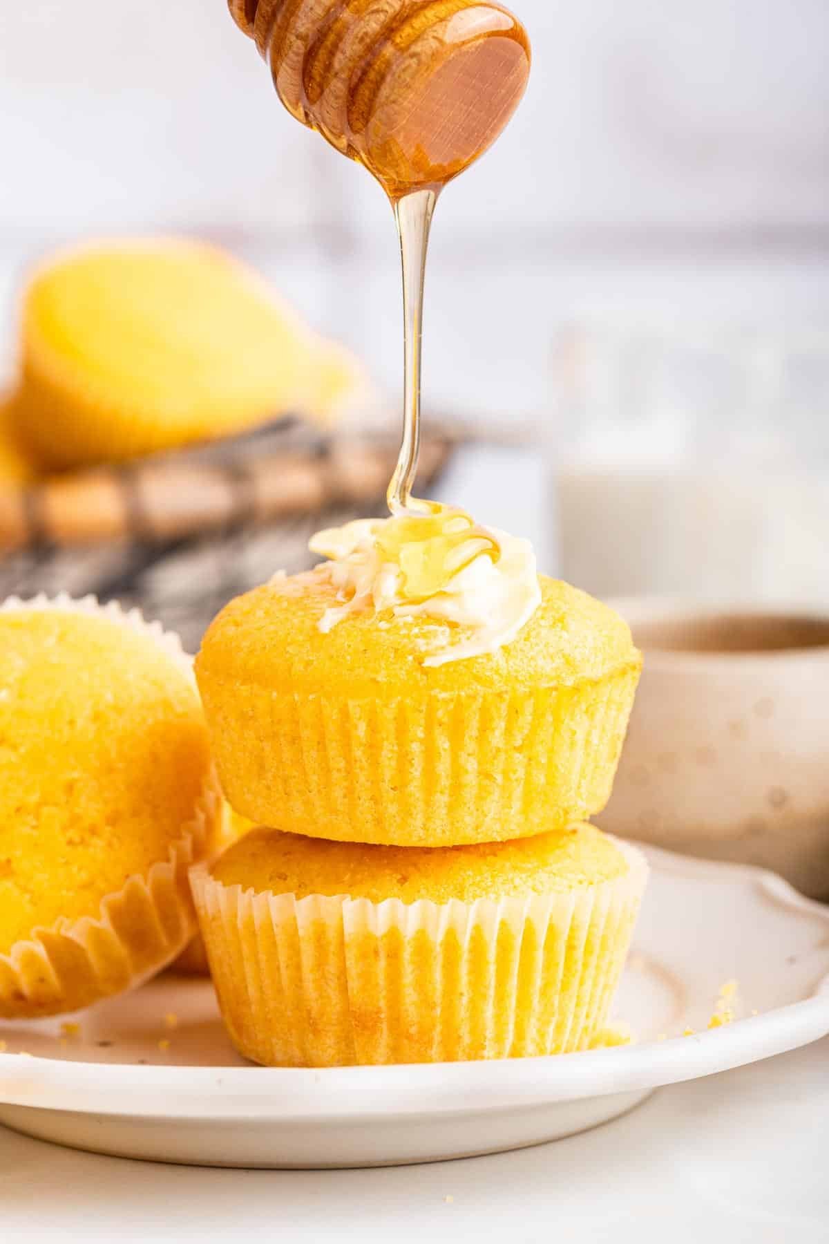 Two yellow corn muffins stacked on top with honey being drizzled on top.