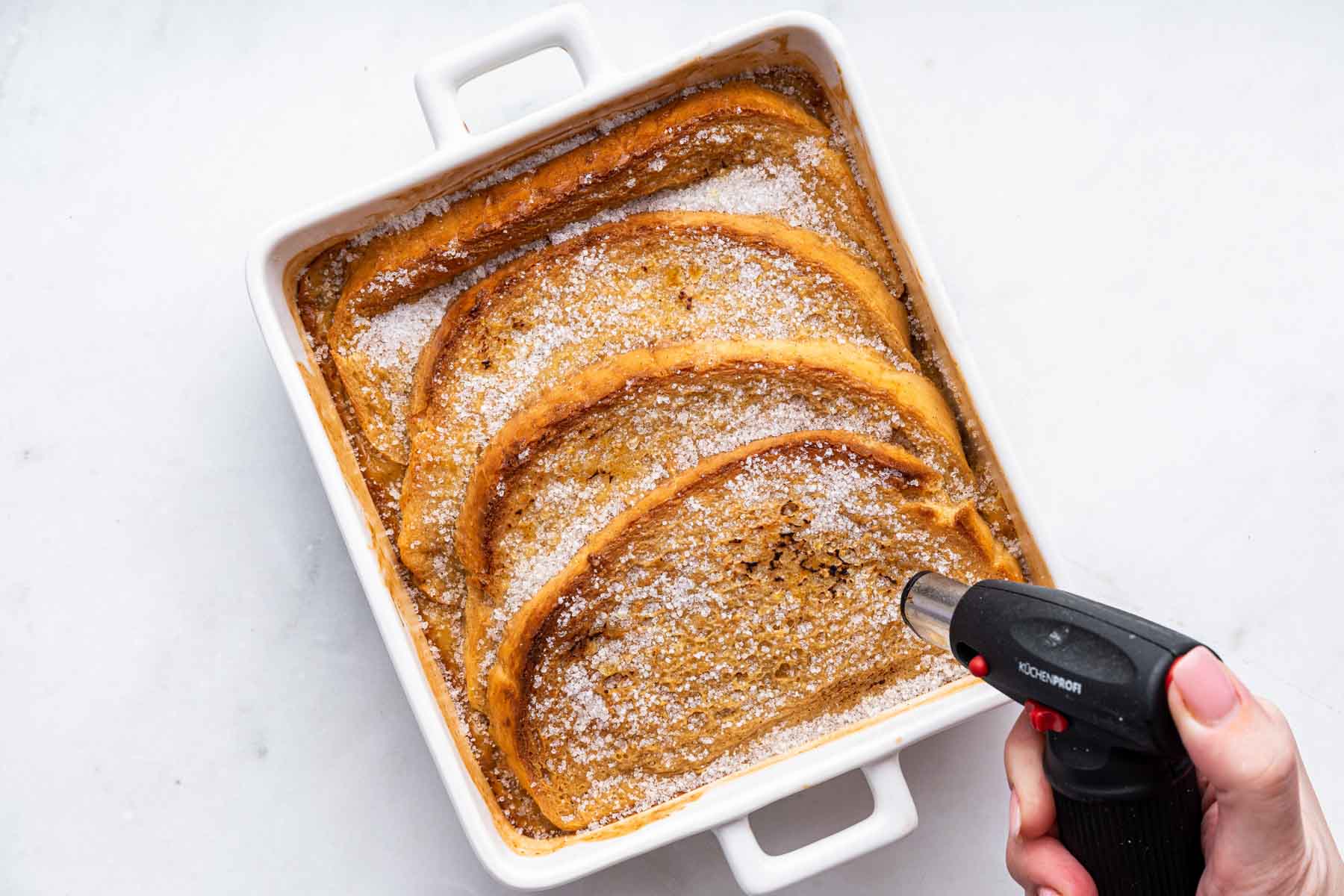 Hand using a culinary torch on bread.