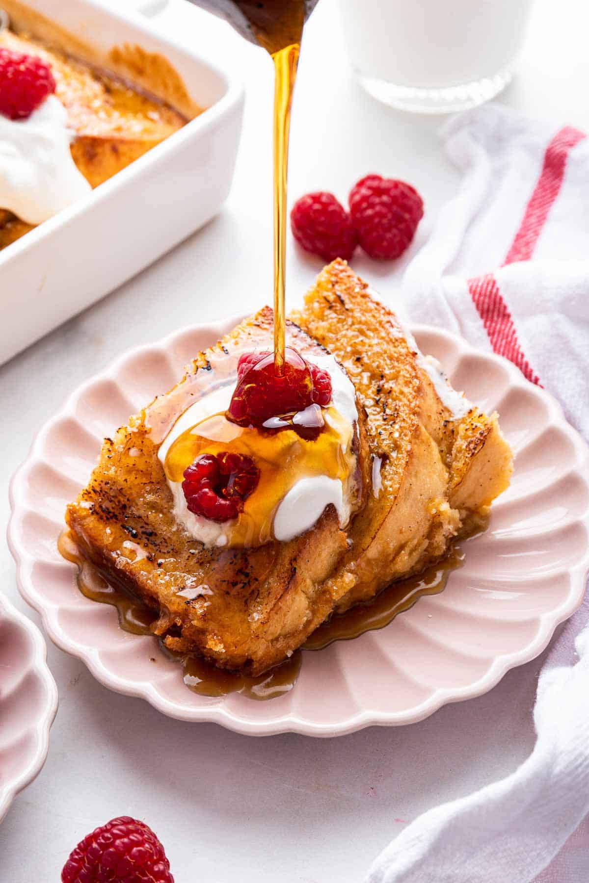 Slice of creme brulee French toast on pink plate with syrup being drizzled on top.