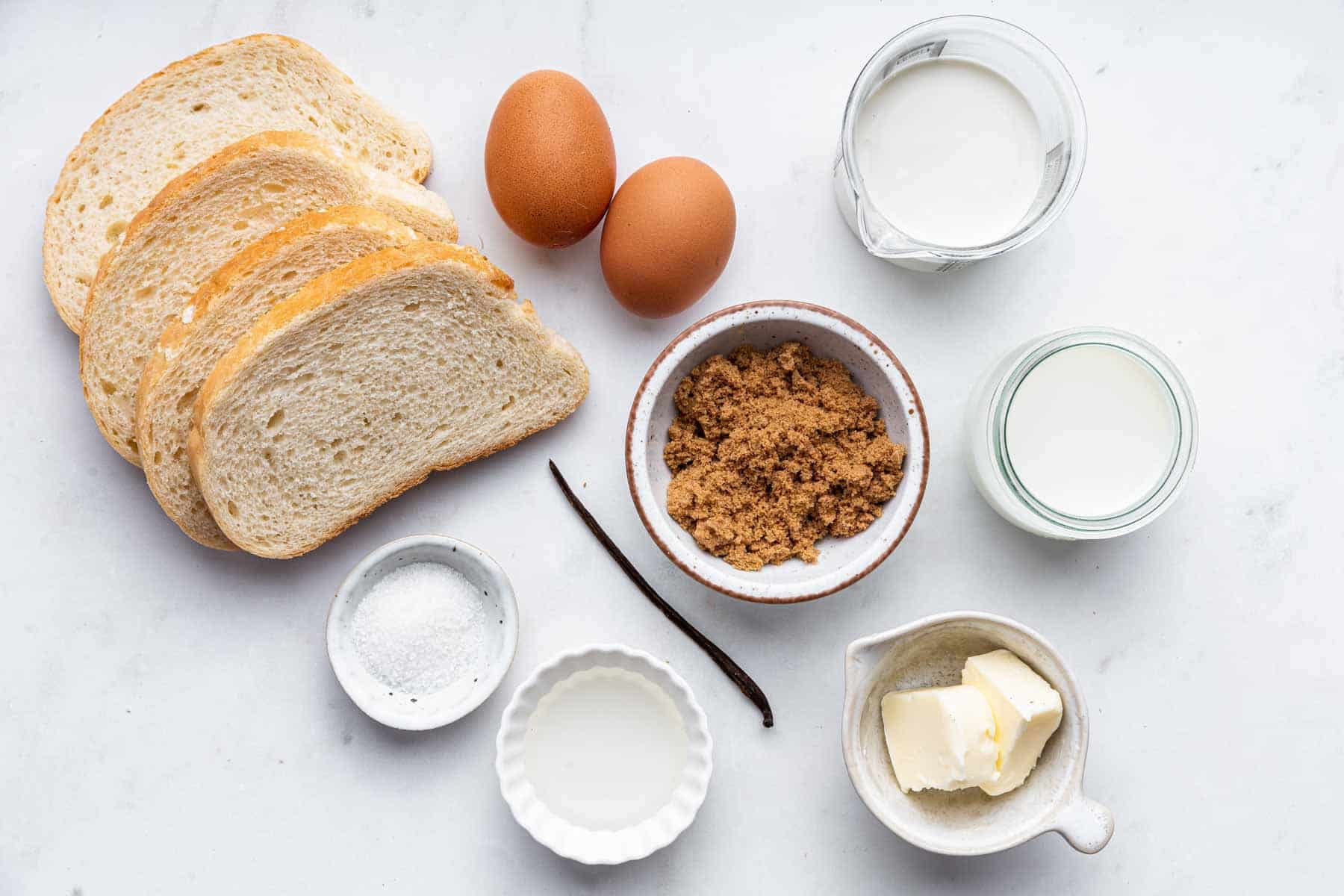 Slices of bread, eggs, brown sugar, and a vanilla bean on kitchen counter.