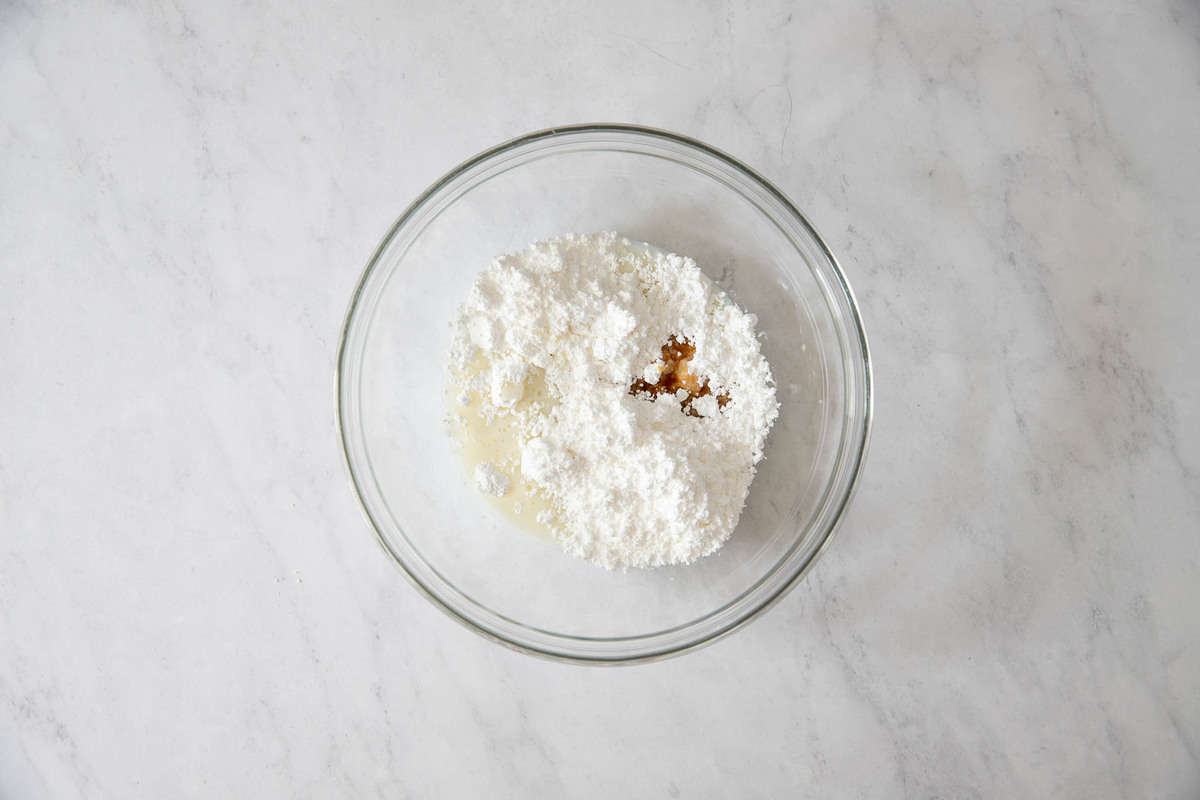 Clear bowl with powdered sugar, milk and vanilla.
