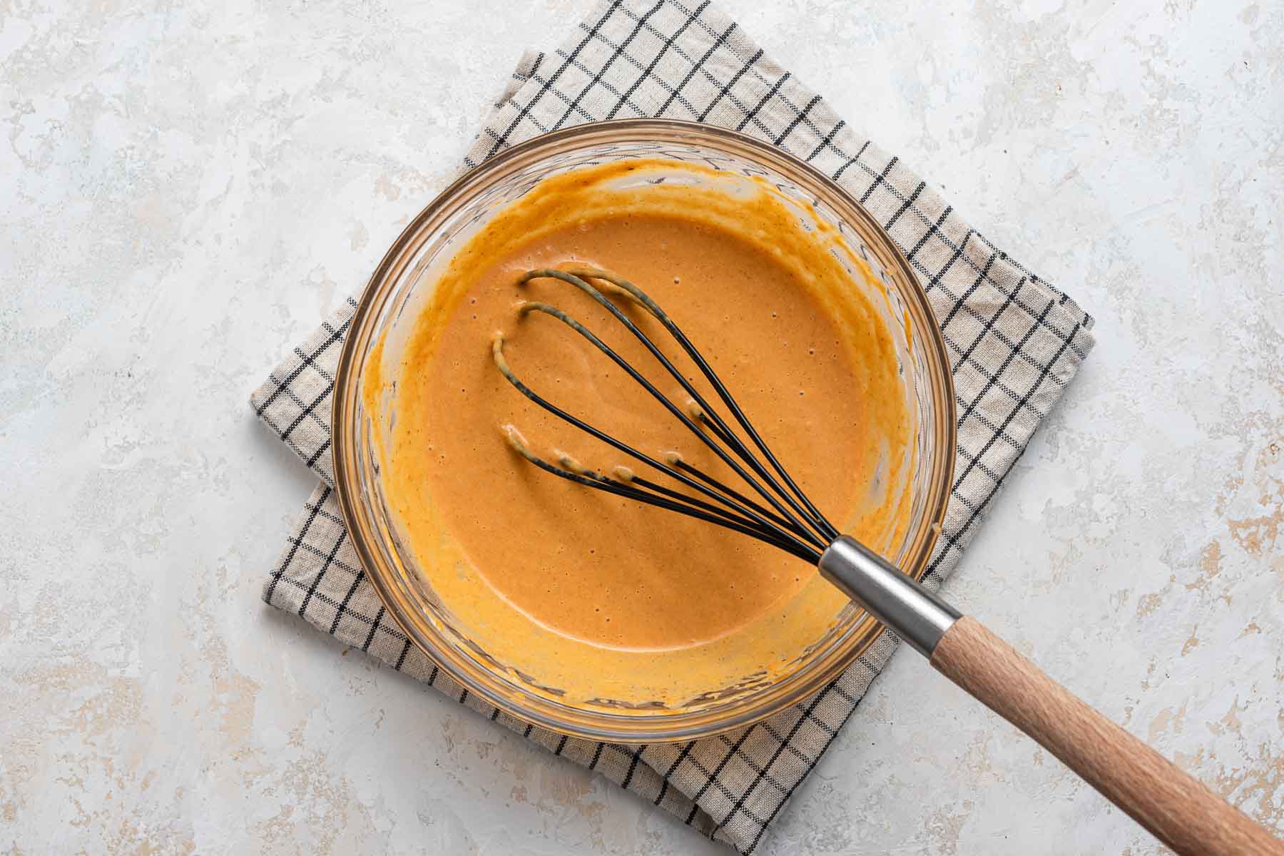 Pumpkin pie filling in clear bowl with whisk.