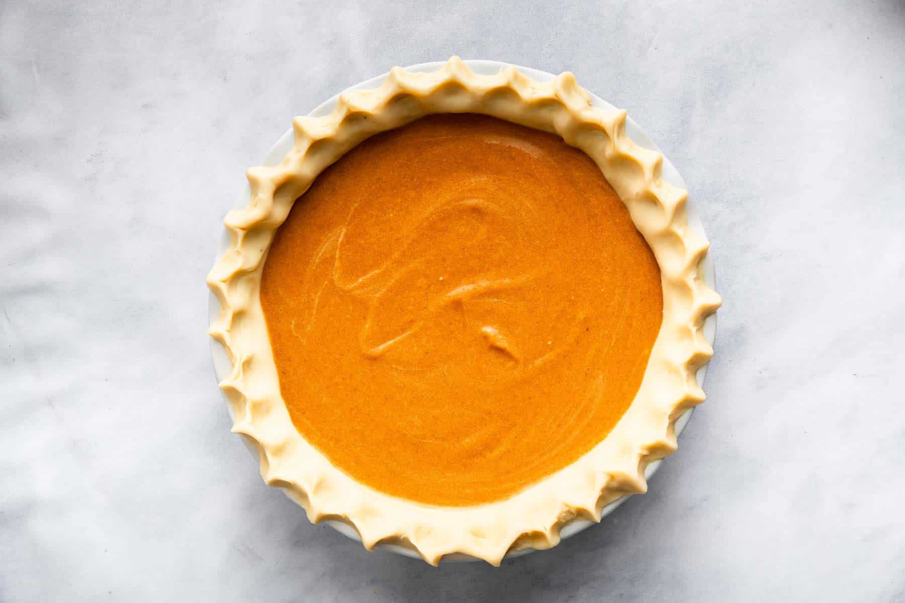 Bright orange custard dessert in a crimped crust on a marble board.