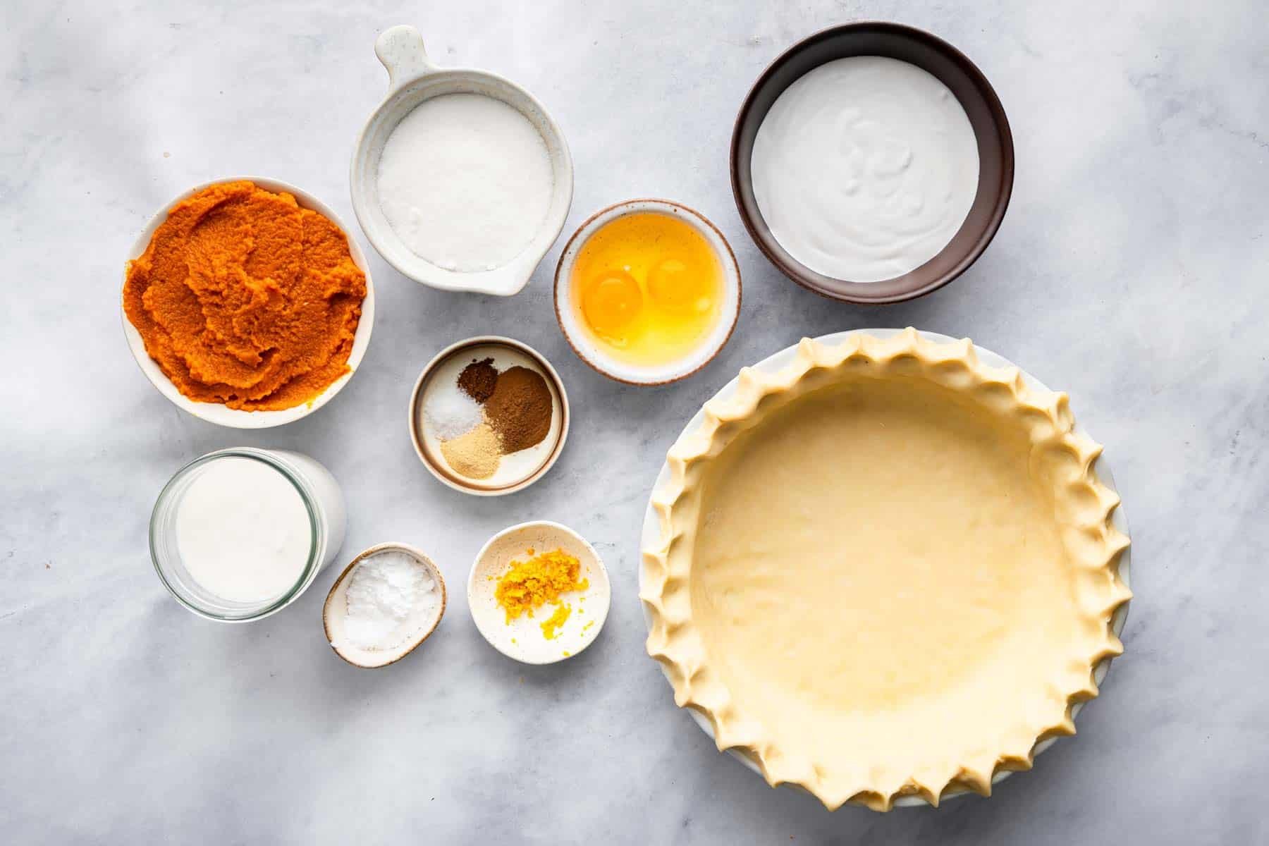 An empty deep dish pie crust and bowls of other baking ingredients.