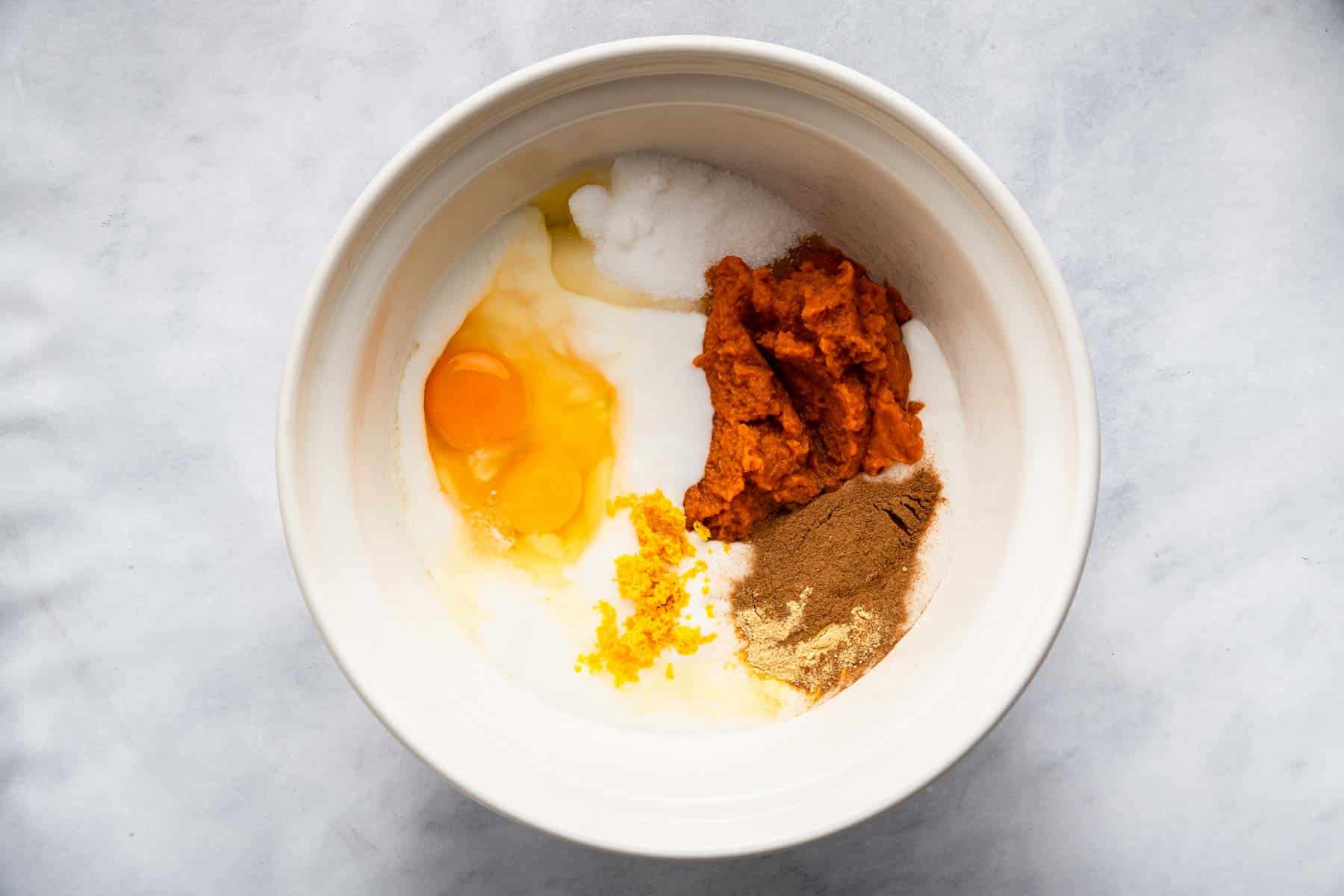 White bowl with eggs, pumpkin puree, spices, and coconut milk.