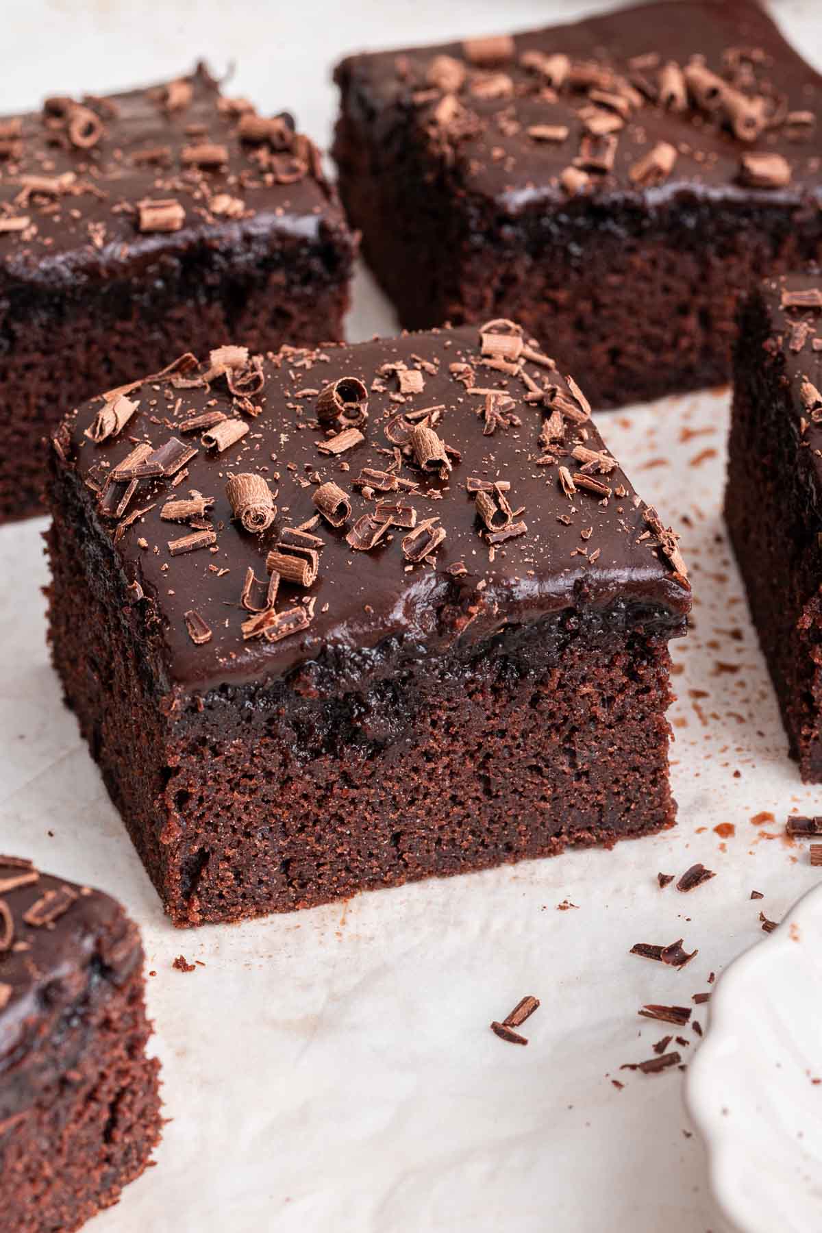 Dr Pepper Cake Square slice of Dr Pepper cake with chocolate shavings on top on white board.