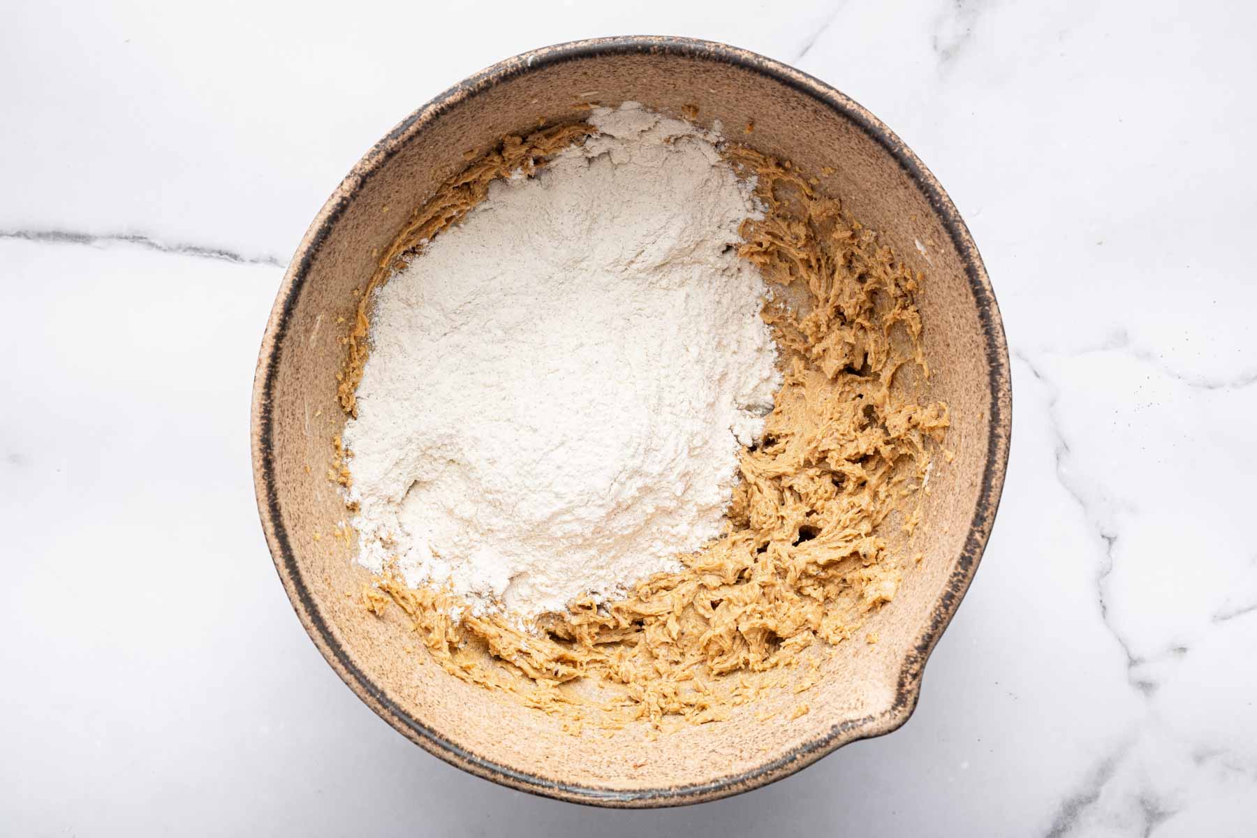 Brown batter with white flour sprinkles on top needing to be stirred in.