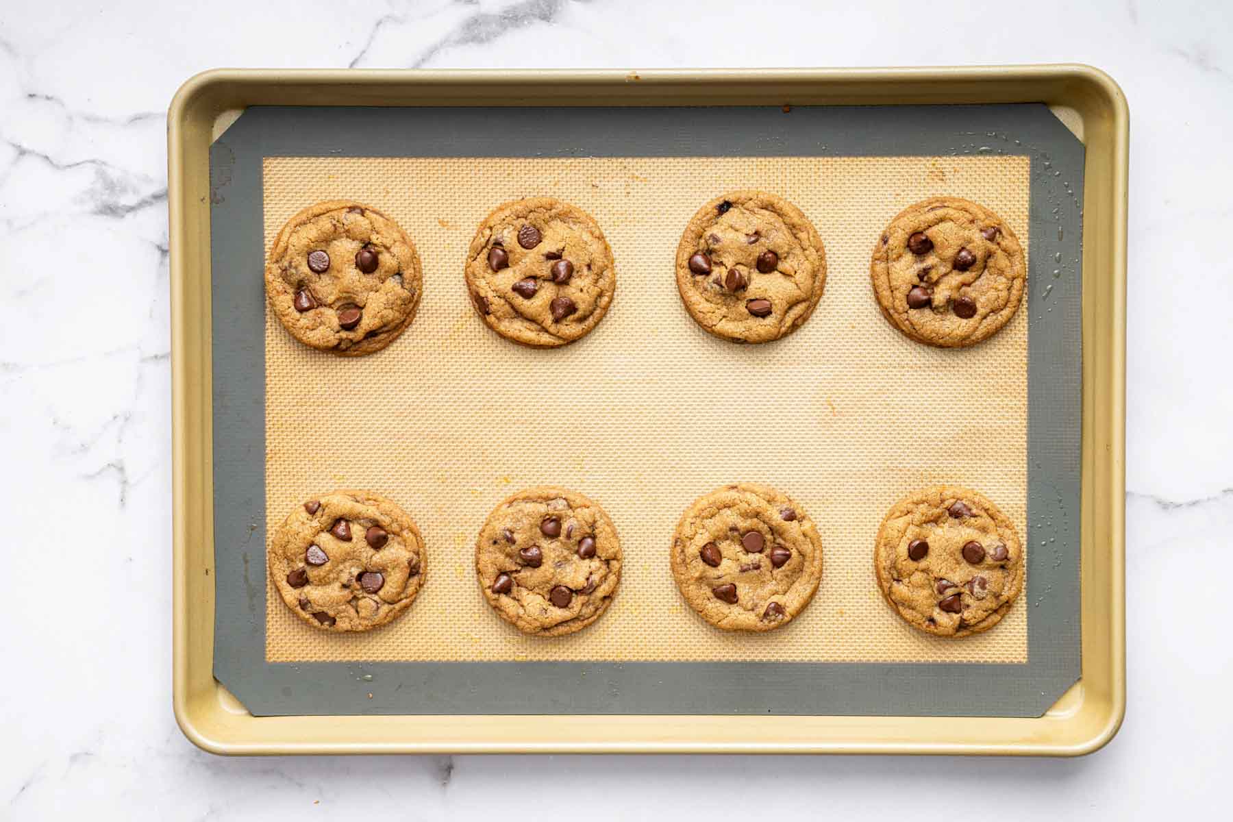 Eight freshly baked eggless chocolate chip cookies on a baking sheet.