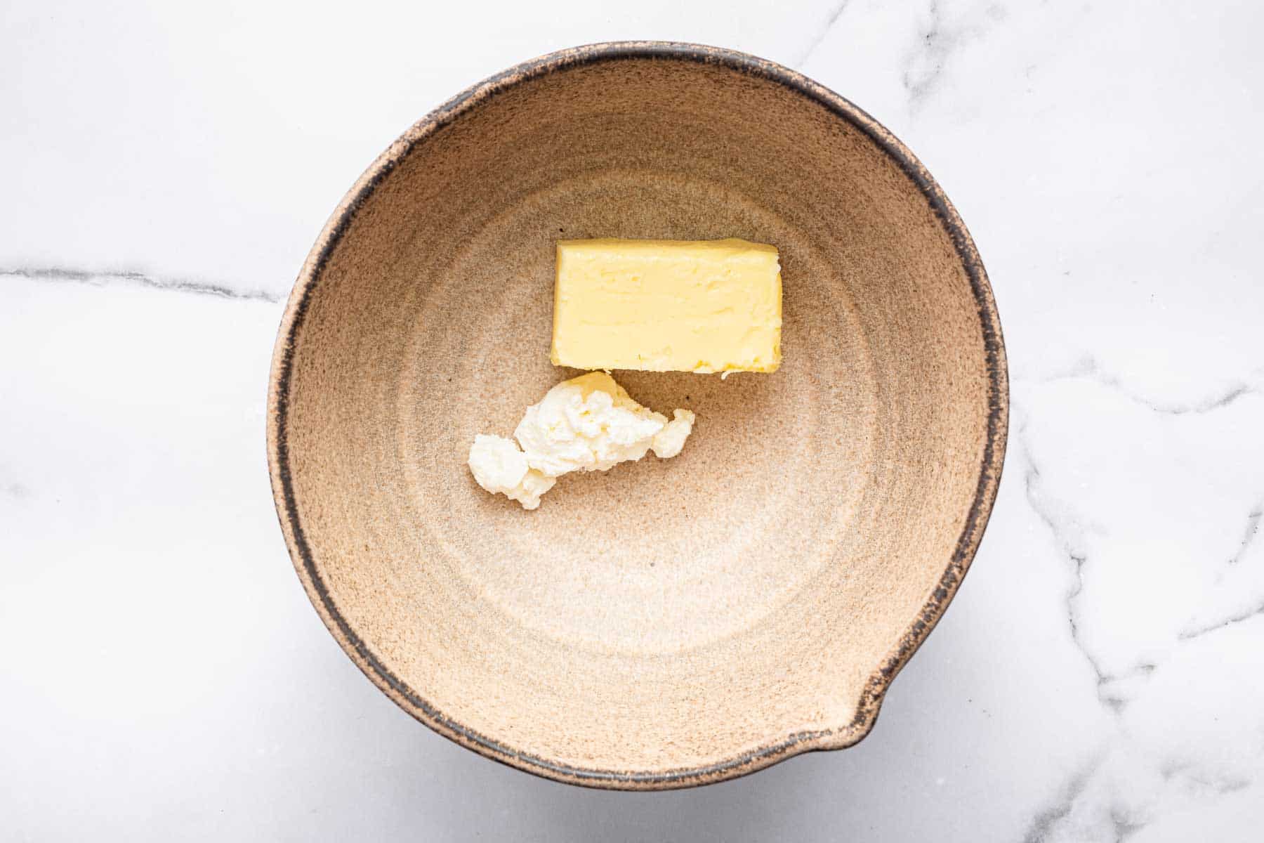 Brown bowl with butter and cream cheese in bottom.