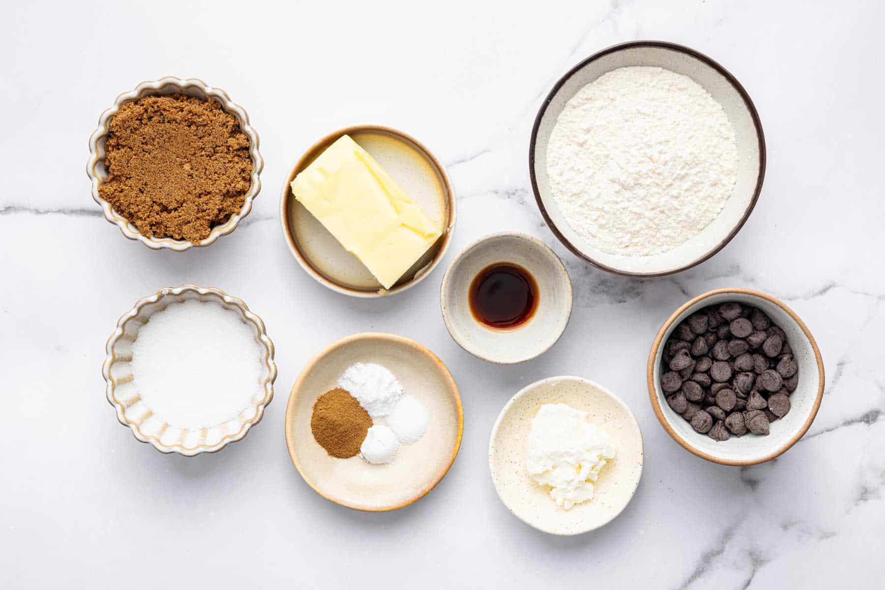 Small bowls with baking ingredients over white marble countertop.
