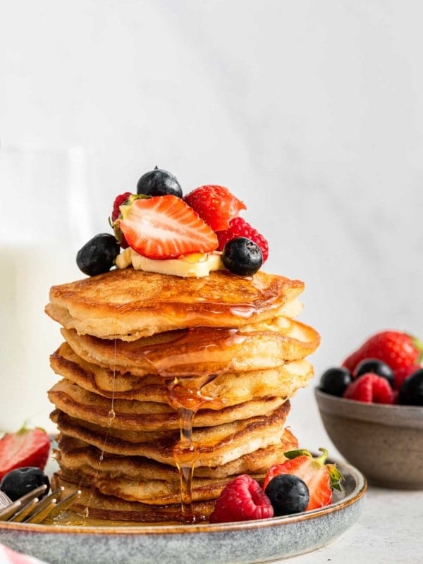 Tall stack of eggless pancakes with fresh fruit and syrup on top.