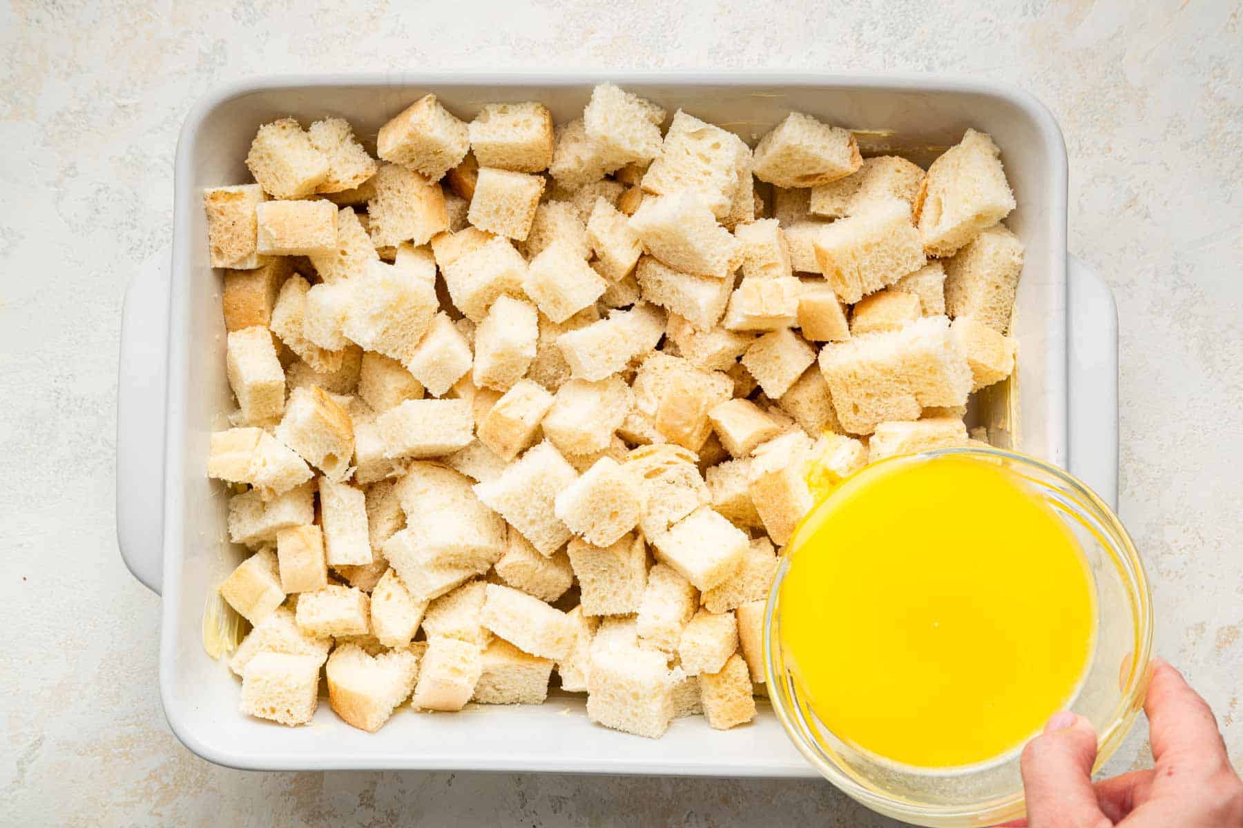 Bread cubes in a rectangular tray with butter being poured on top.