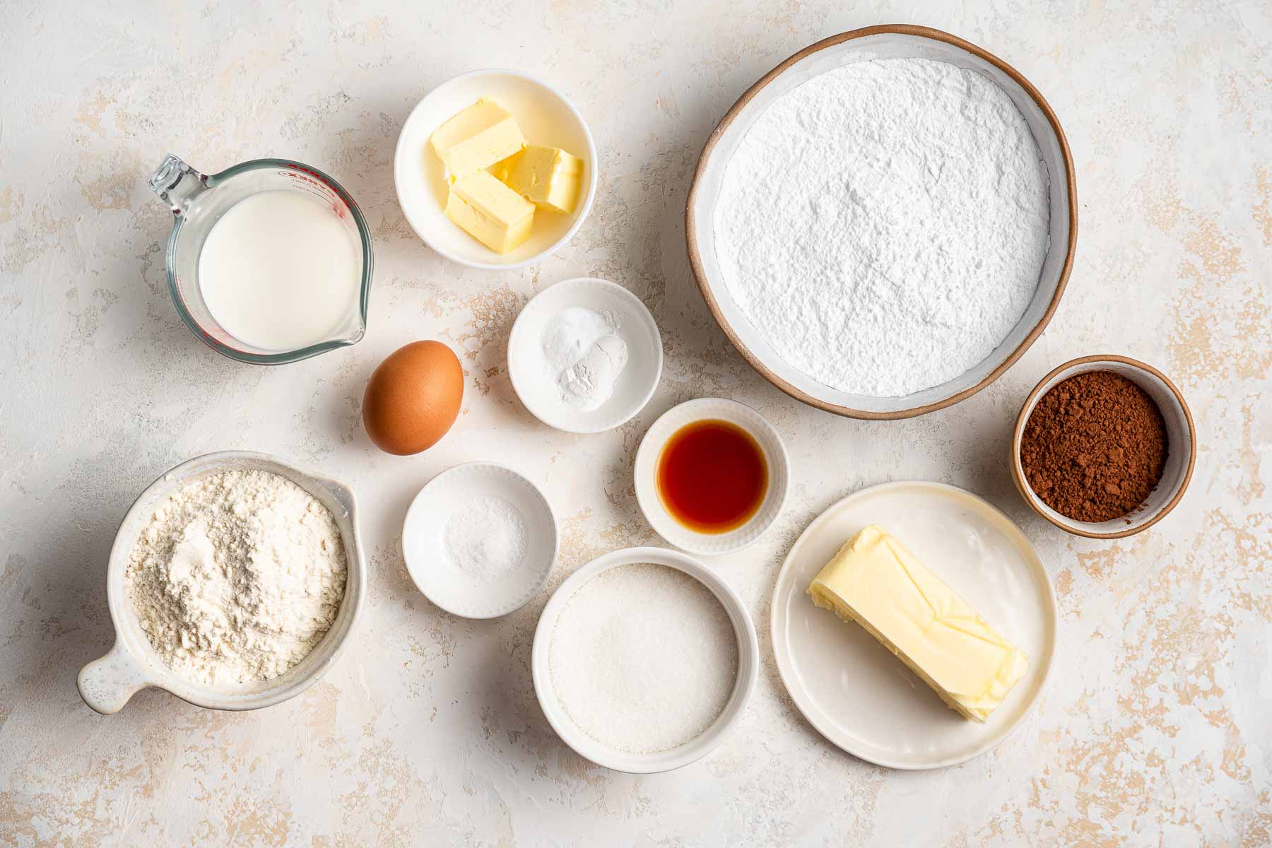 Ingredients for cupcakes in little bowls on marble surface.