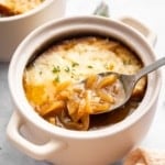 Bowl of French onion soup with spoon removing a scoop.