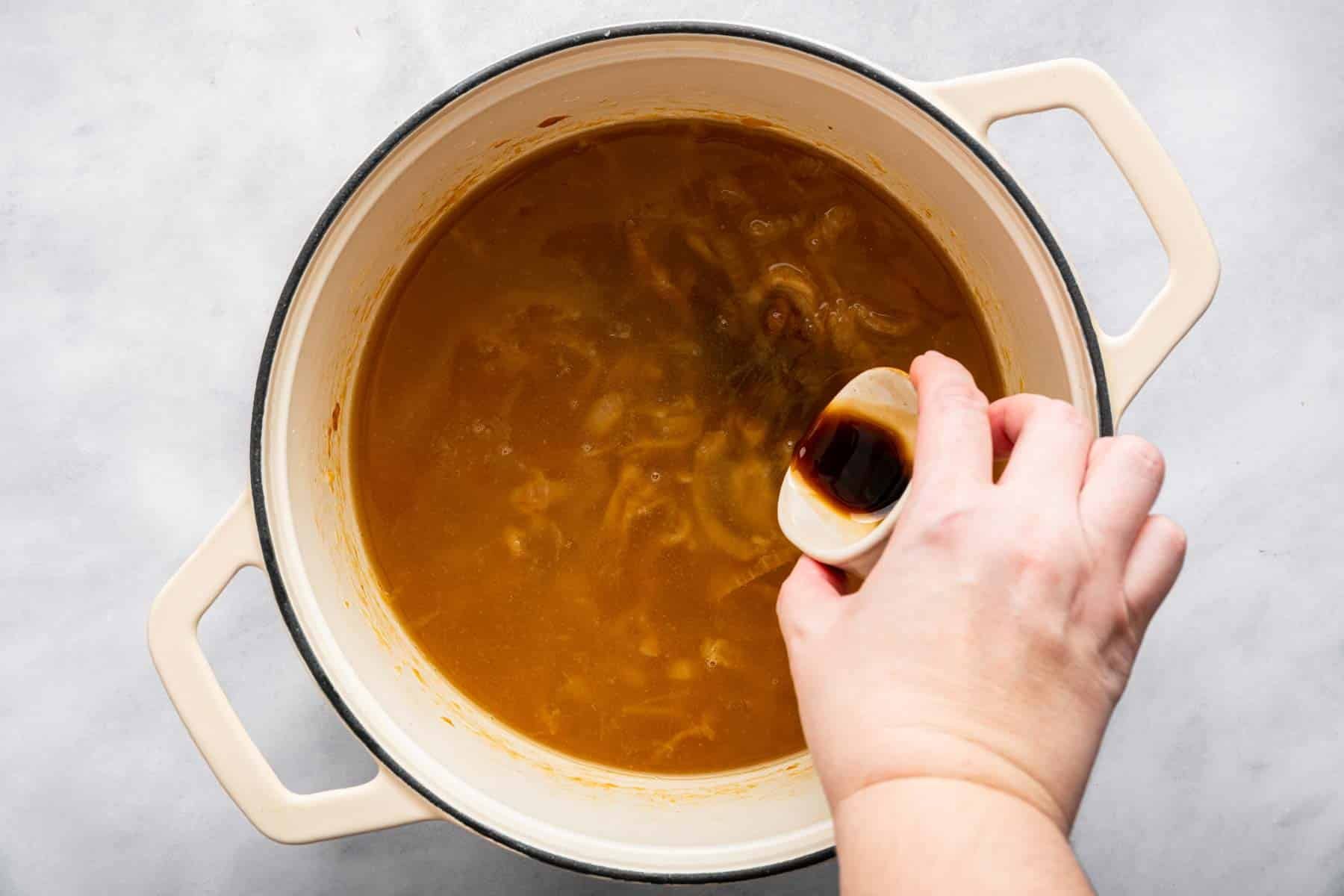 Hand pouring brown soy sauce into a brown soup.