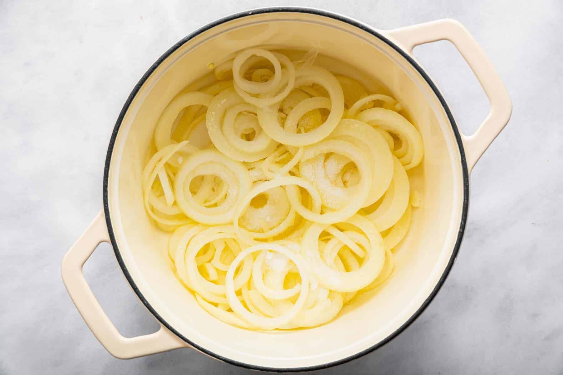 Sliced onion rings cooking in butter in a white pot.