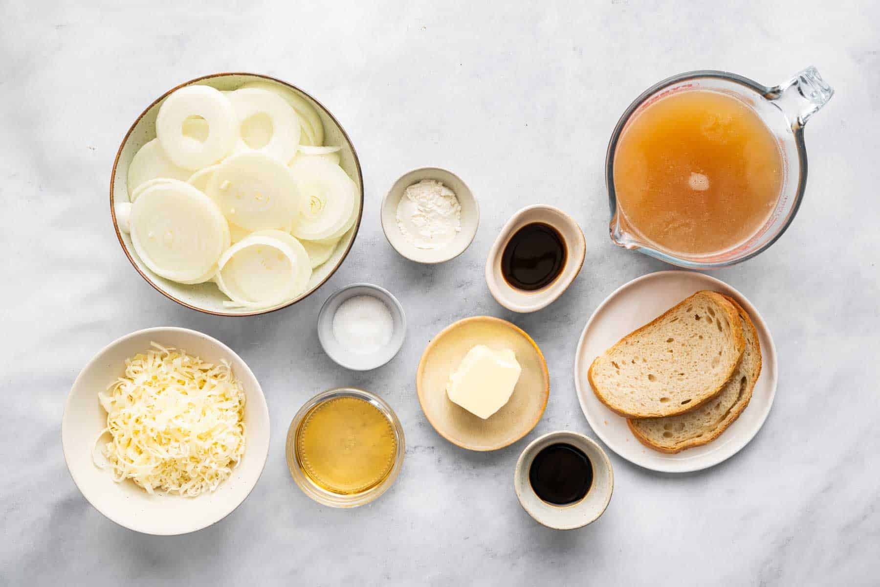 Bowls of sliced veggies, broth, sauce, and sliced bread.
