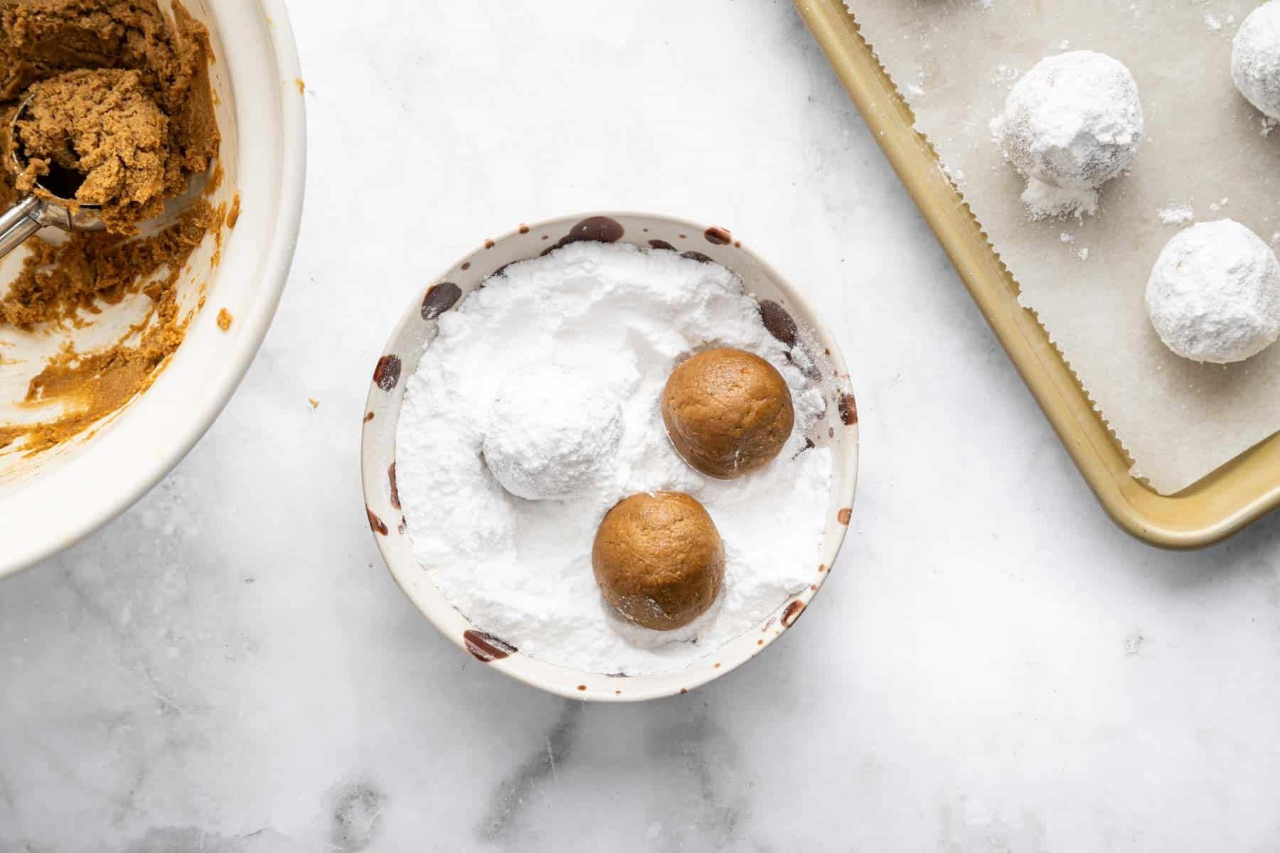 Three brown dough ball being rolled in powdered sugar on a small plate.