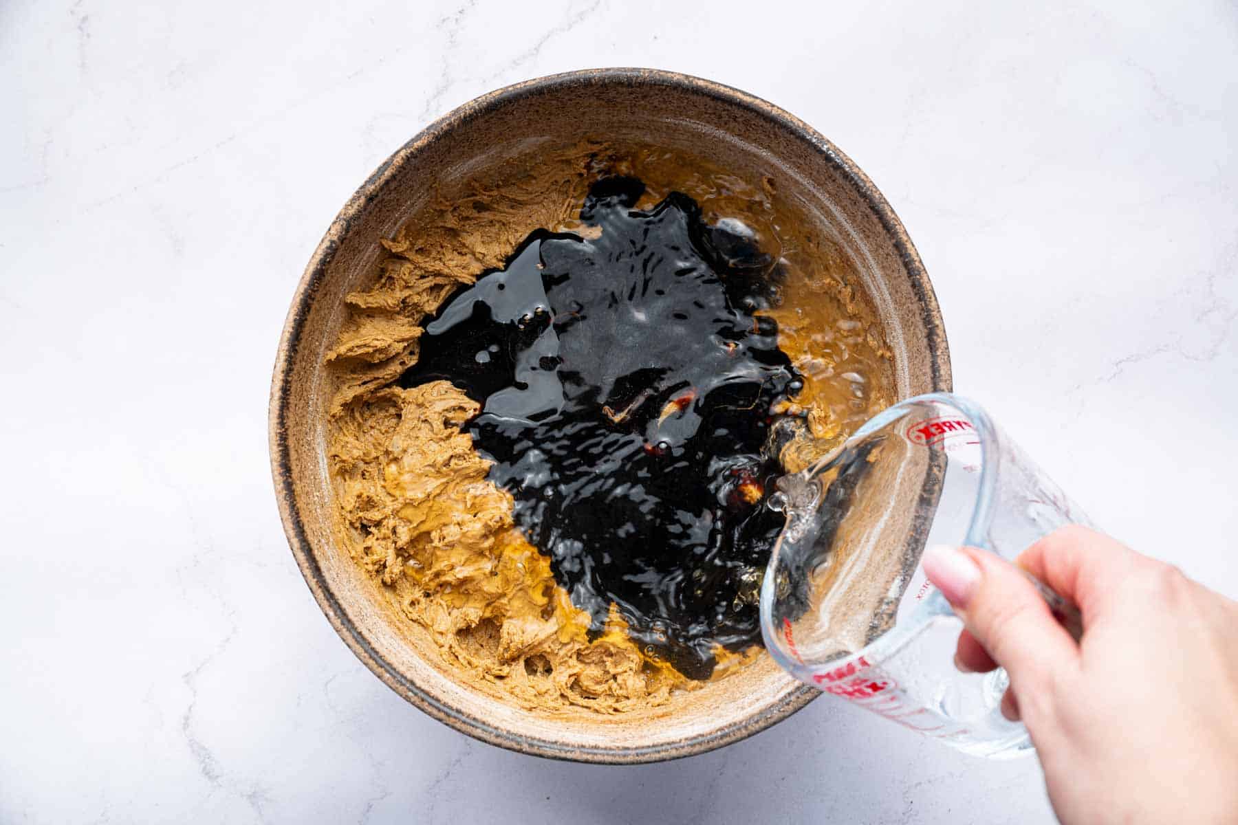 Hand pouring molasses over batter in a bowl.
