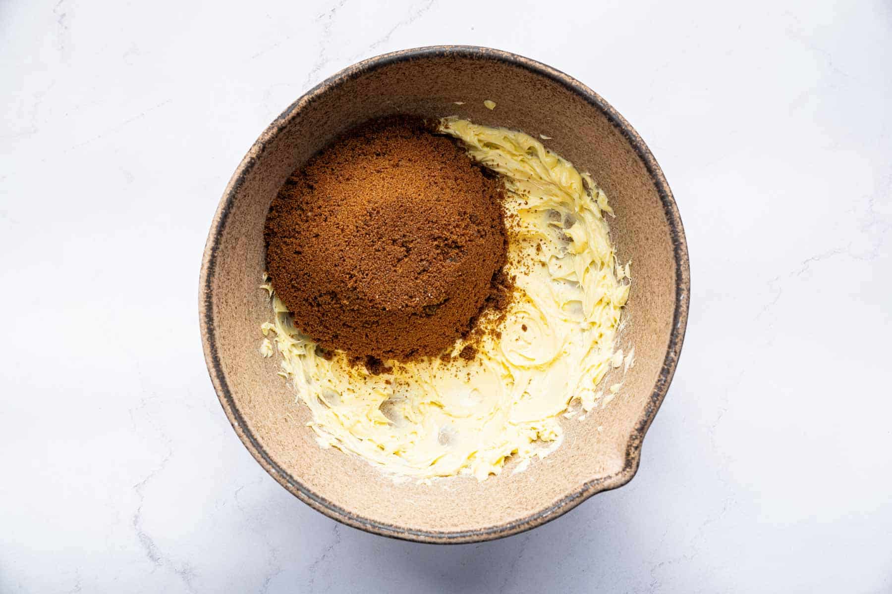 Bowl with creamed butter and a scoop of dark brown sugar on top.
