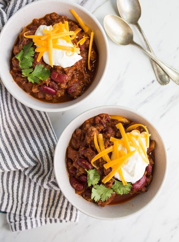 Overhead shot of two bowls of red chili garnished with sour cream and grated cheese.