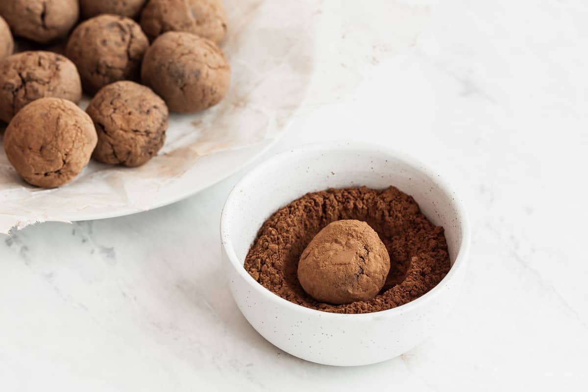 Chocolate truffle in small bowl of cocoa powder.