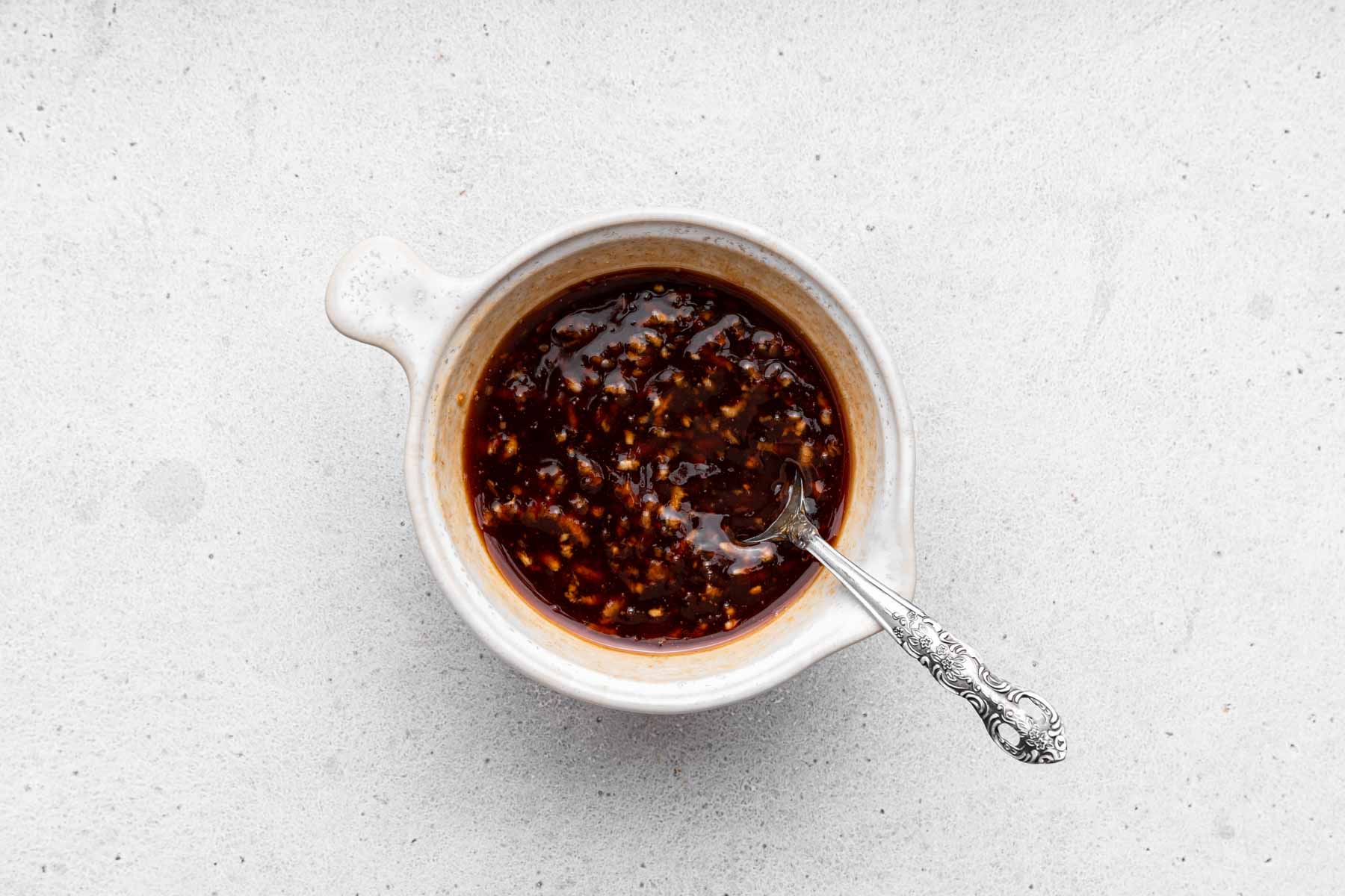 Black syrupy sauce with garlic pieces in white bowl with fork.