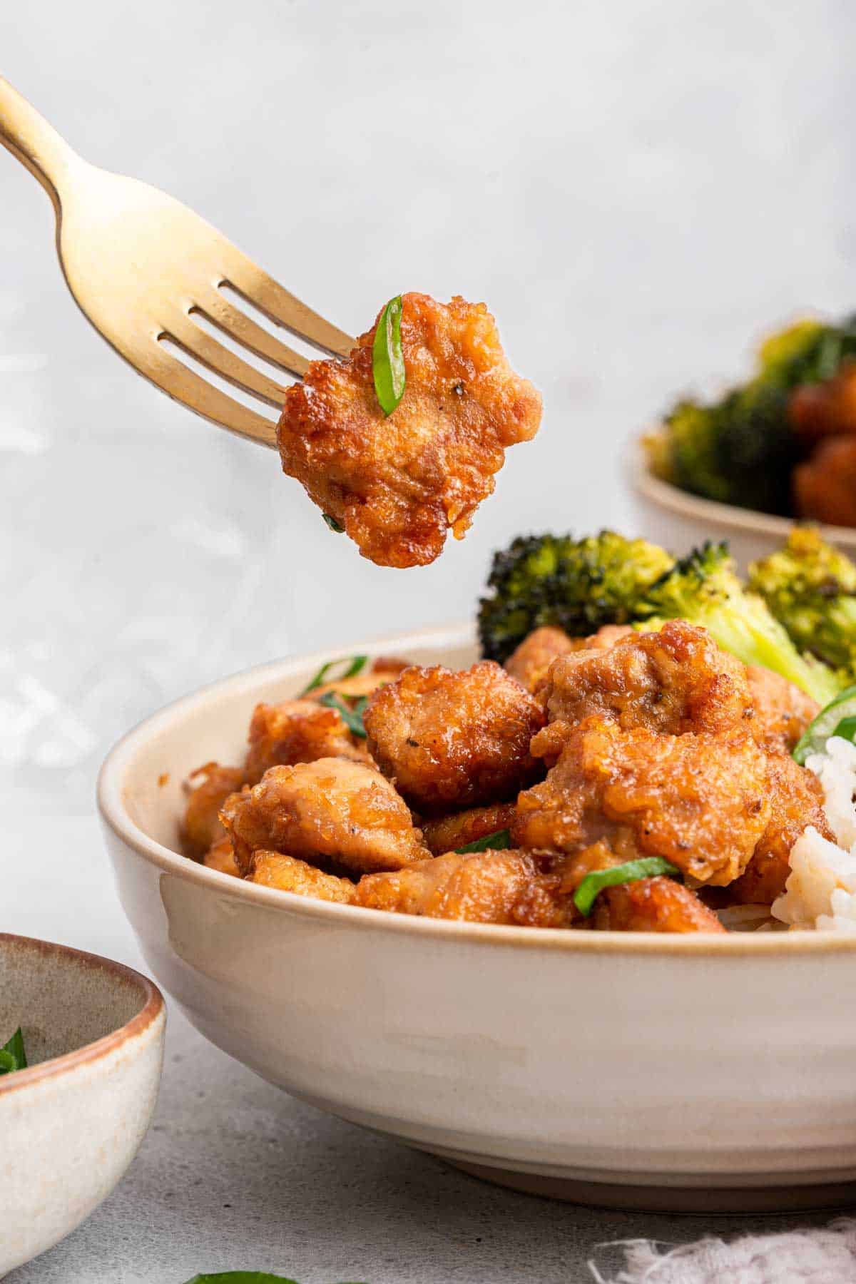 Bowl of fried honey garlic pork with one piece on a fork above bowl.