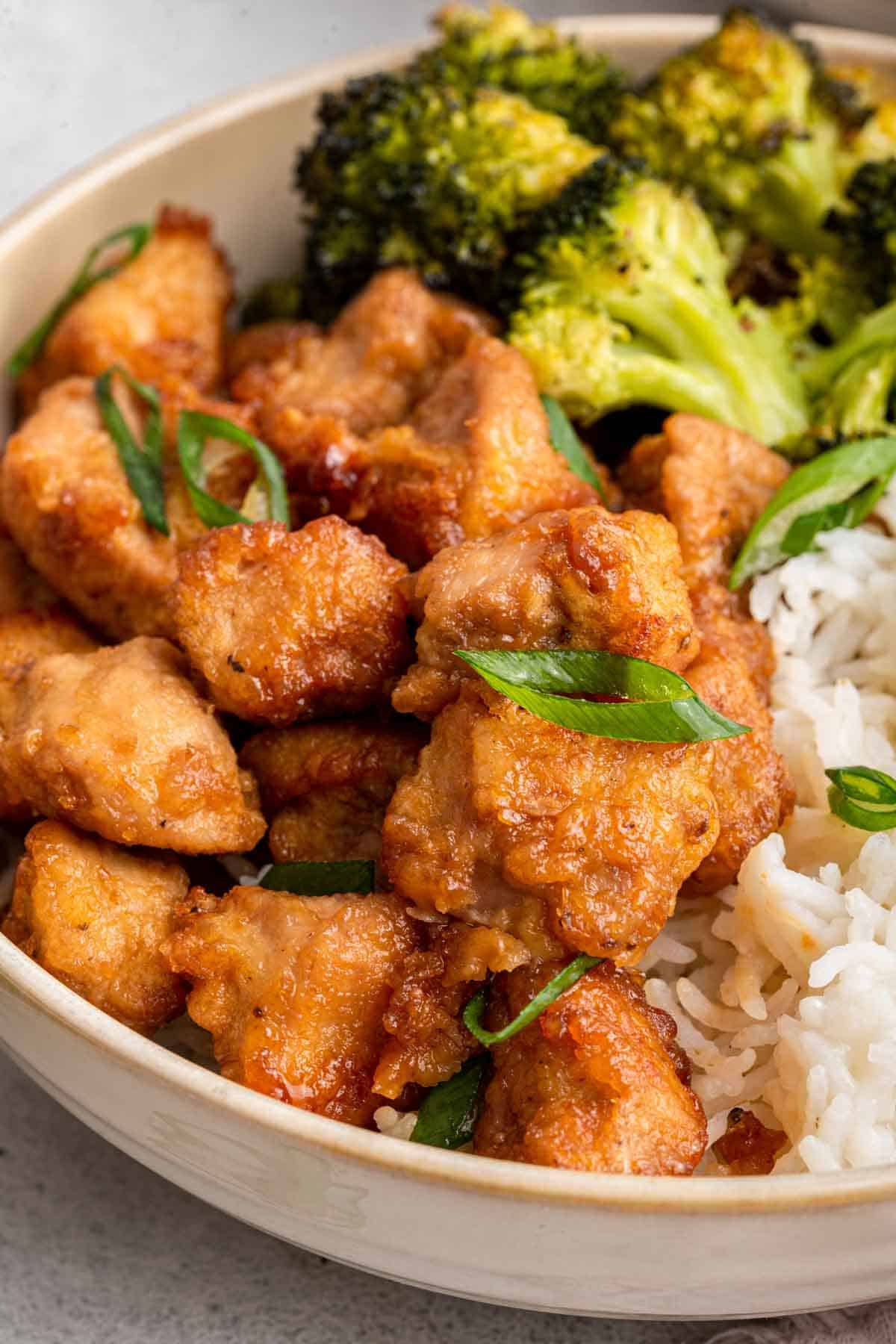 Close up of honey garlic pork in bowl with broccoli and rice on the side.
