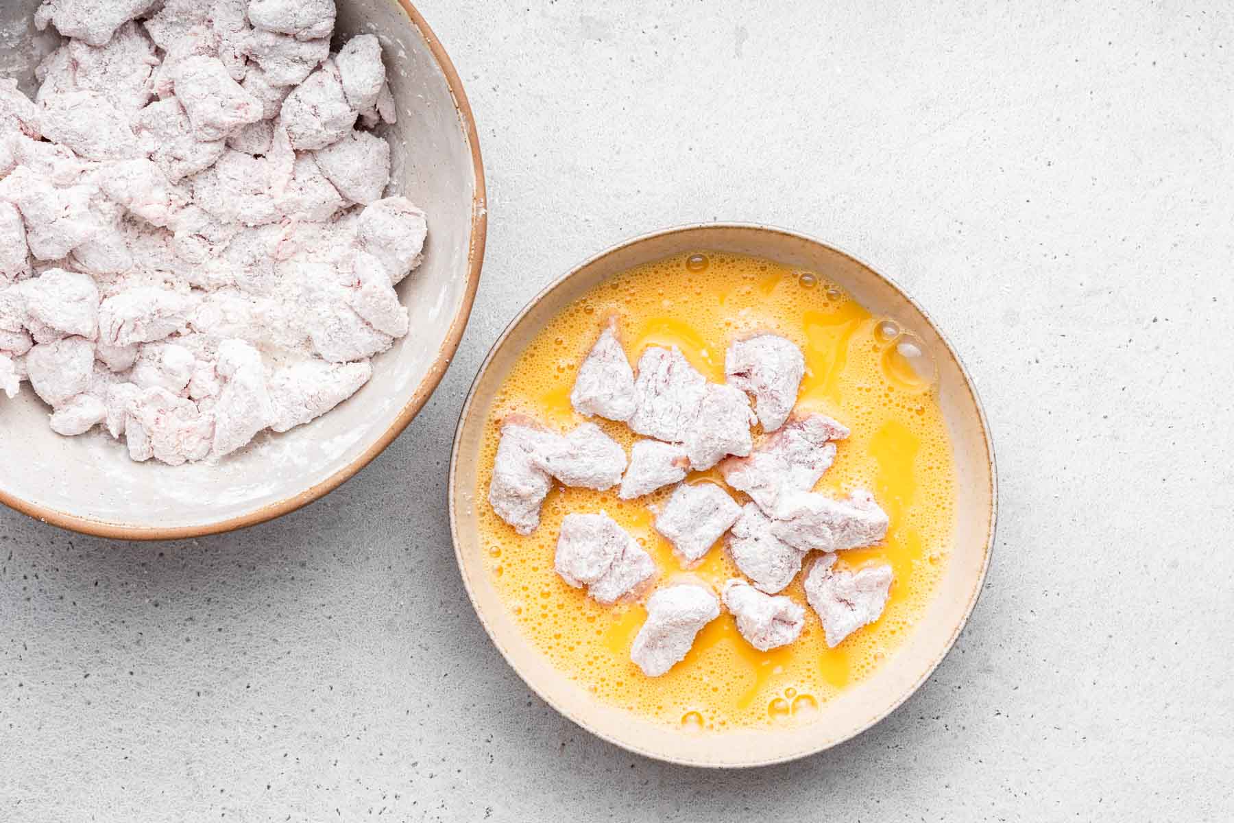 Bowl of meat pieces coated in cornstarch and being dipped in yellow egg.