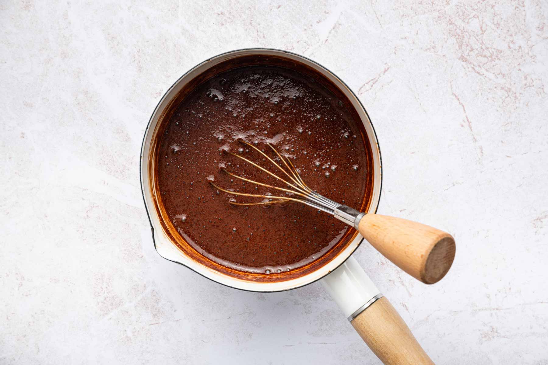 Brown sauce in small white pan with whisk.