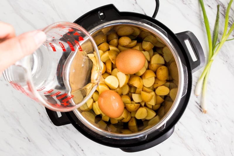 Hand pouring water into pressure cooker with potatoes and eggs.